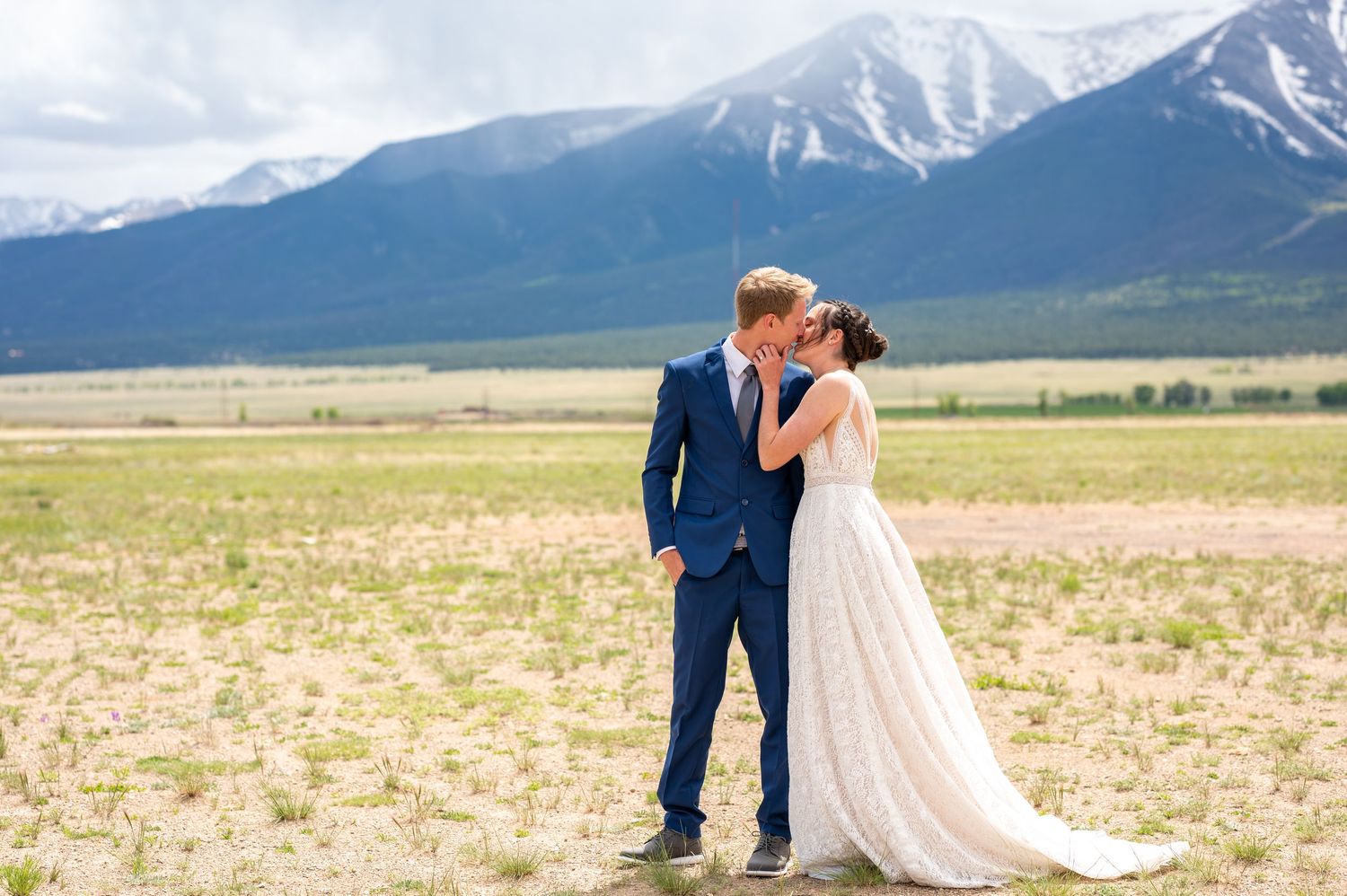 A couple shares a tender moment in a field with snow-capped mountains creating a majestic backdrop.