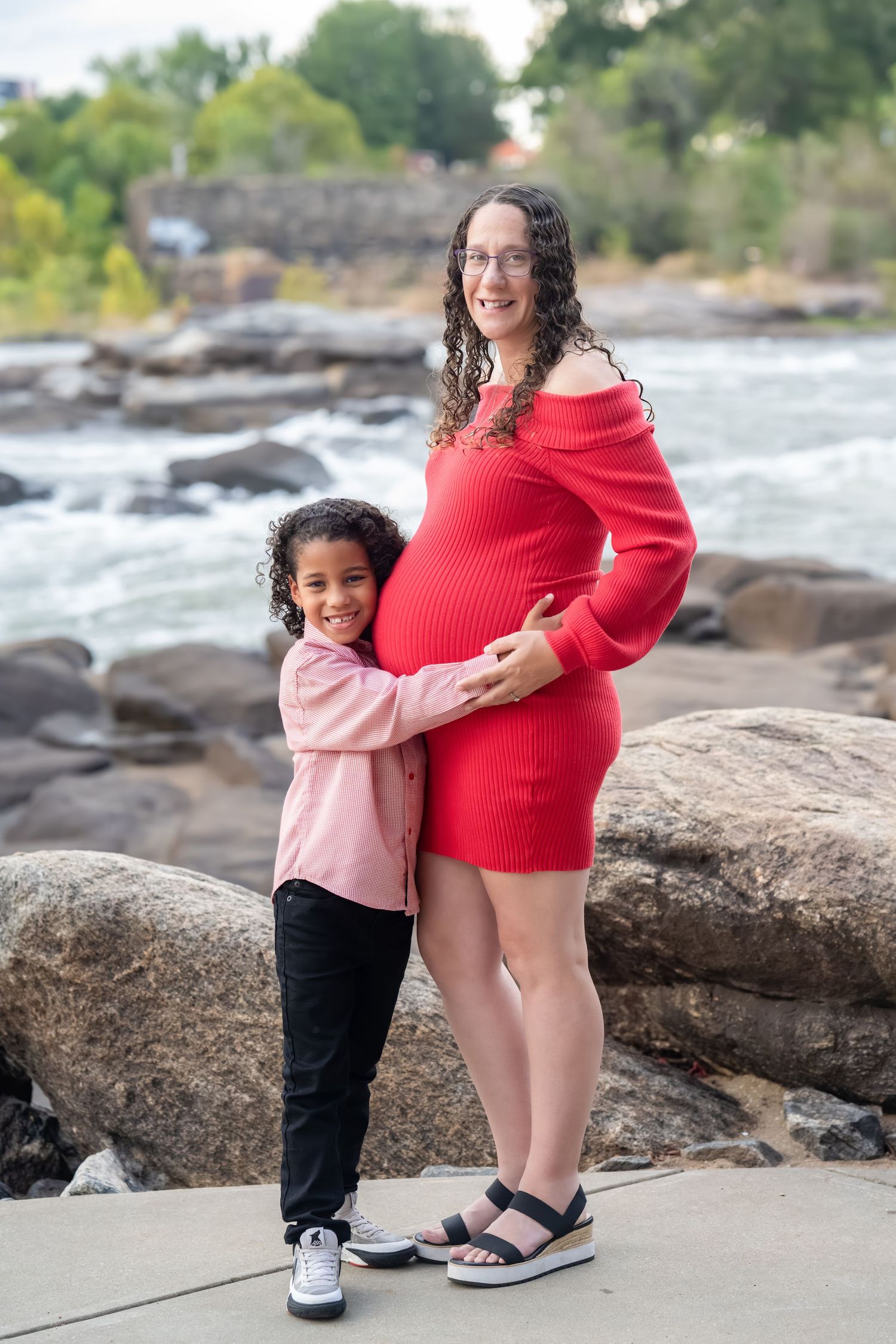 Family maternity photos taken on rocky riverbank showing close-up of feet and embraces.