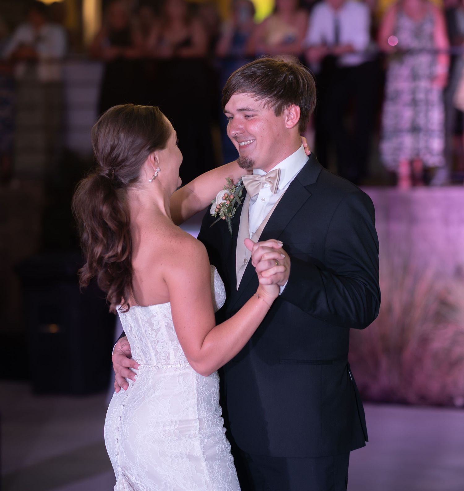 Couple sharing their first dance on an illuminated dance floor during evening wedding reception.
