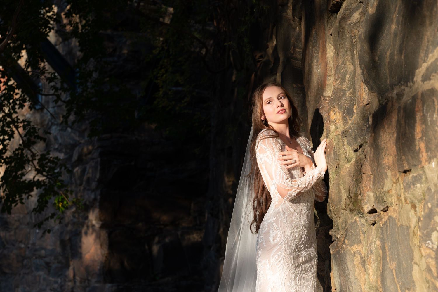 Dramatic bridal portrait against textured rock wall with lace wedding gown.
