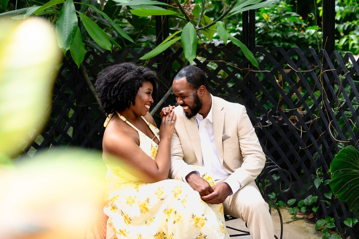A couple shares a tender moment seated together in a lush green garden setting.