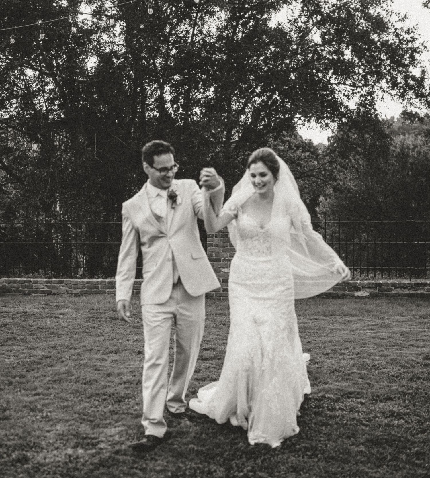 A black and white sequence of a wedding couple, bride and groom, dancing playfully in a field.