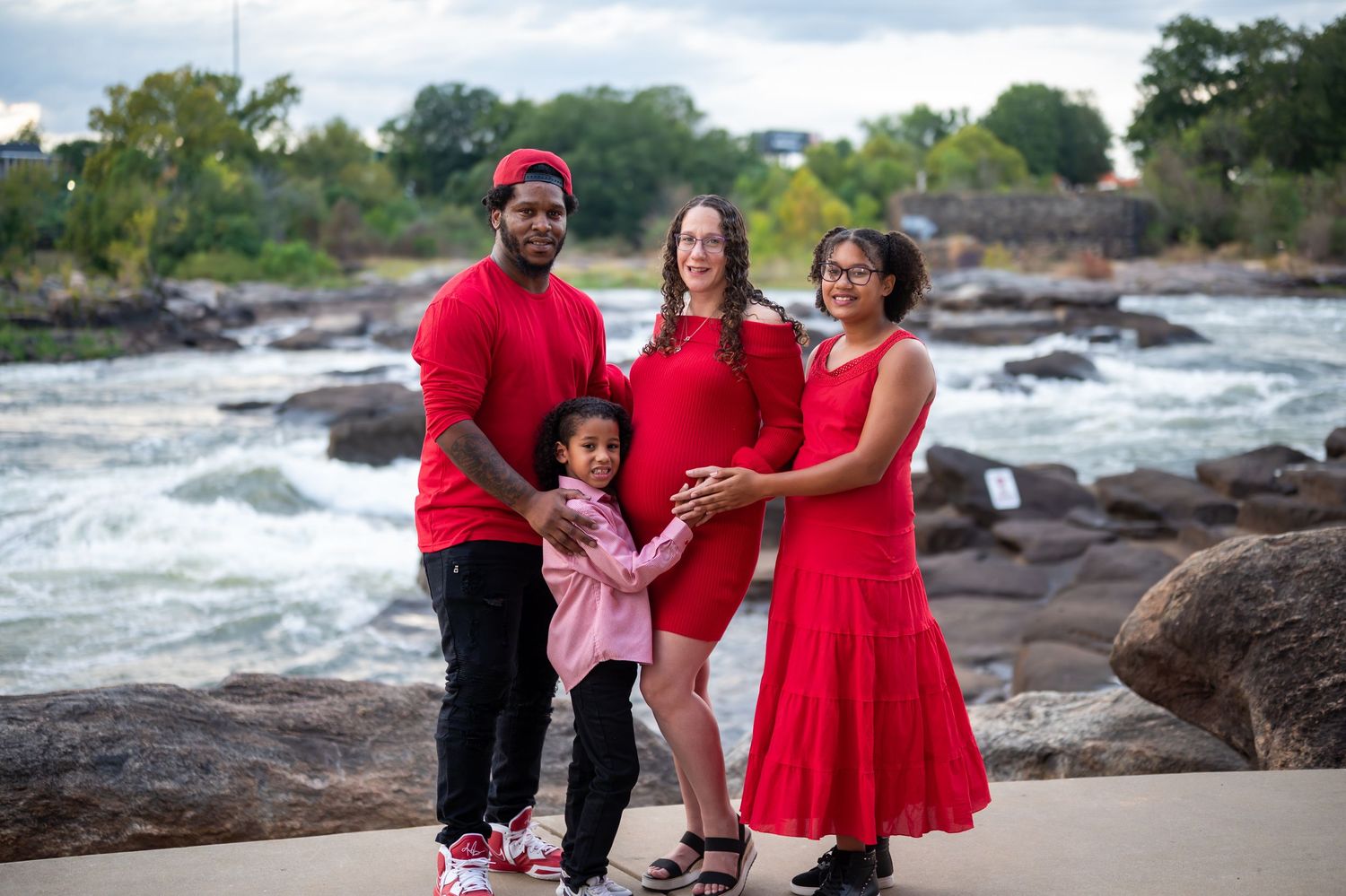 Family portrait session on rocky riverbank with everyone dressed in bright red and black coordinated outfits.