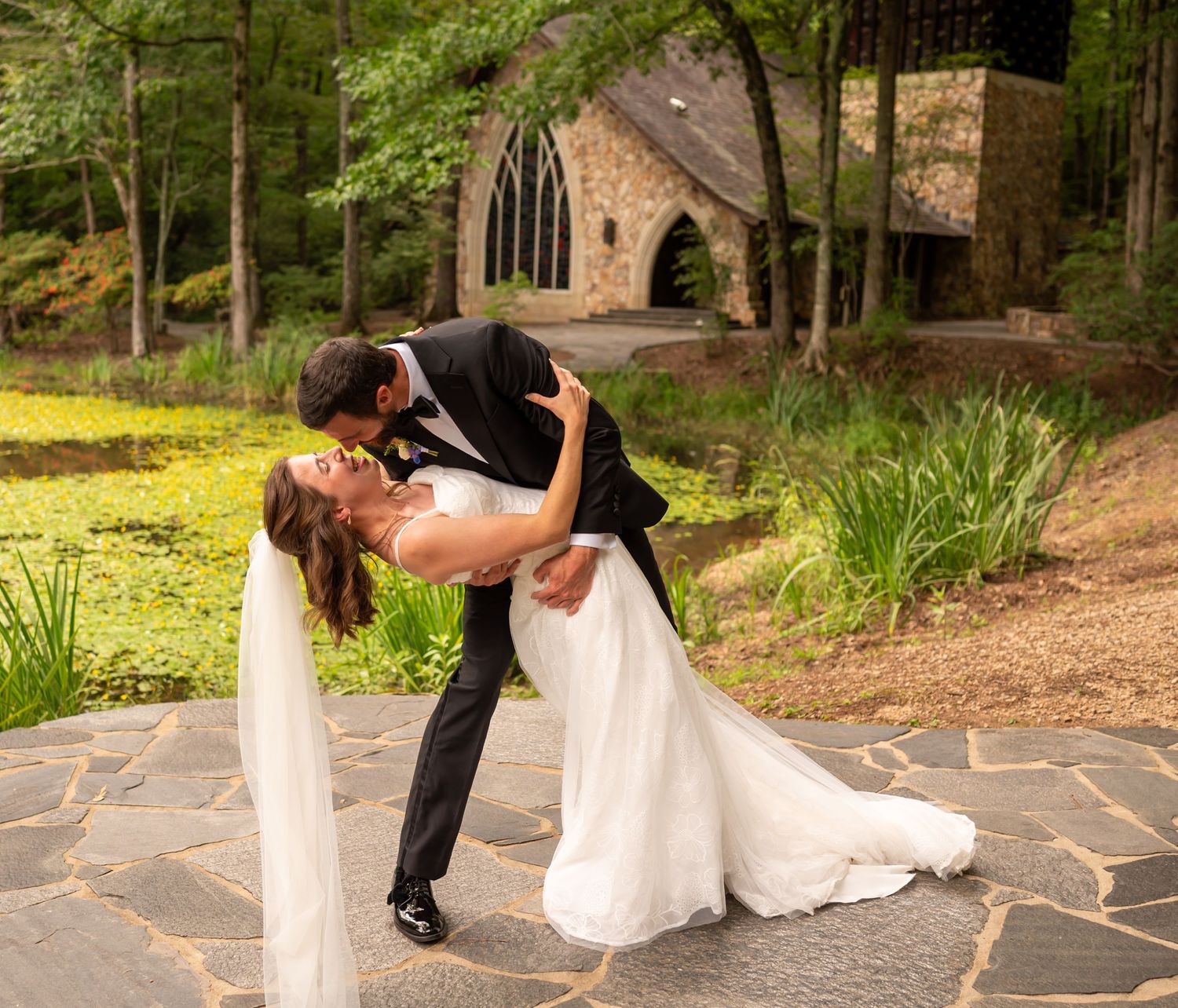 Wedding couple shares romantic dance poses on stone pathway near chapel.
