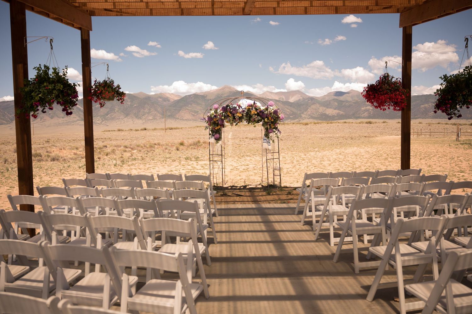 Desert wedding ceremony setup with white chairs and floral arch against mountain backdrop.
