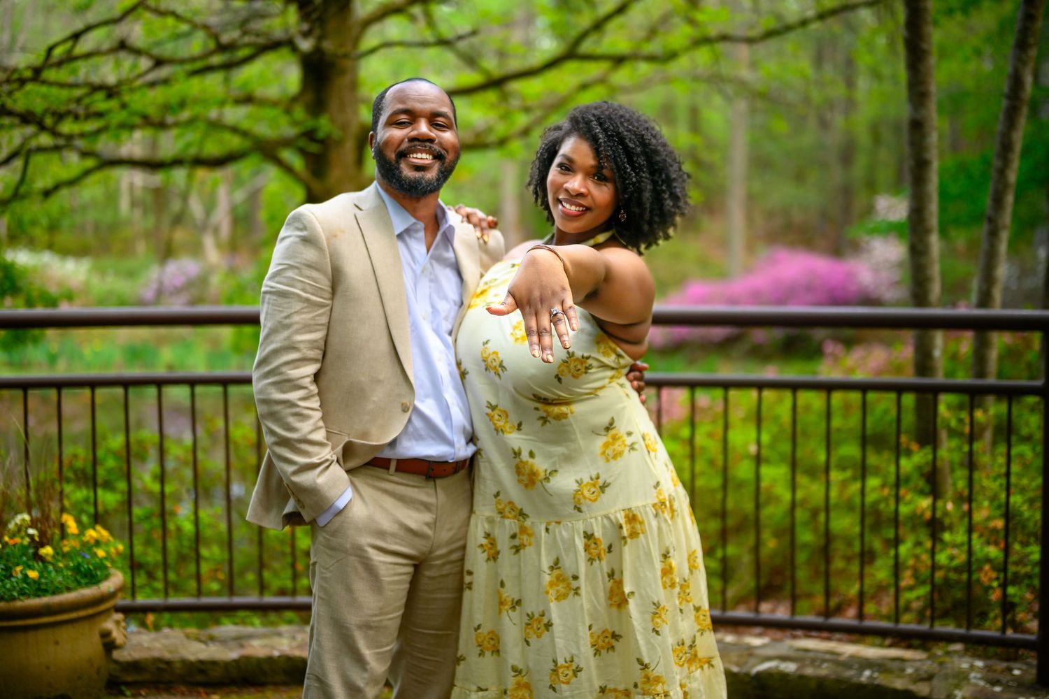 Smiling engaged couple poses together on a garden terrace with colorful blooms in the background.