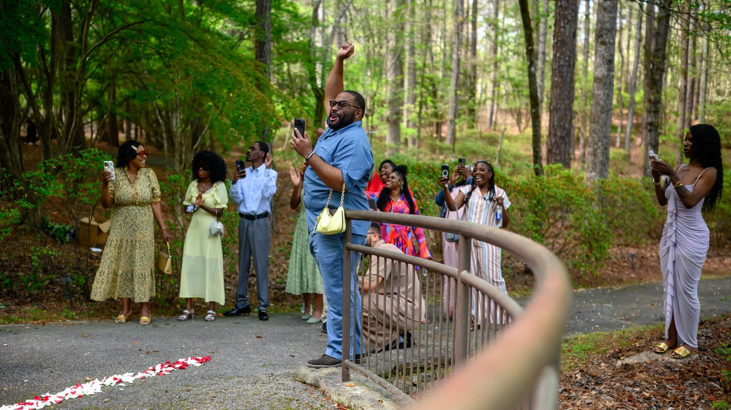 Excited family members celebrate and take photos along a railed garden path surrounded by tall trees and rose petal decorations.