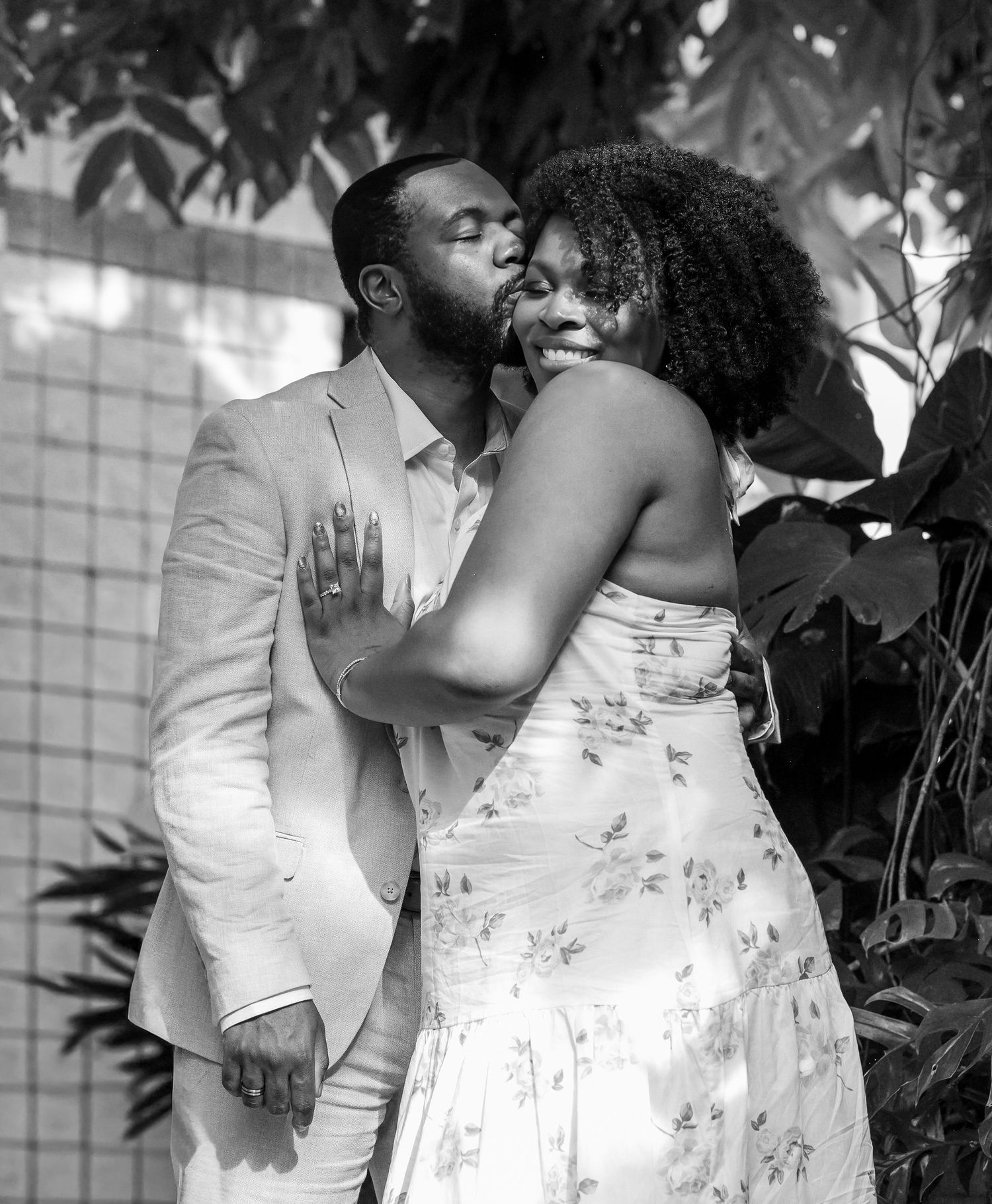 Black and white photo of couple sharing a tender kiss surrounded by lush tropical foliage.