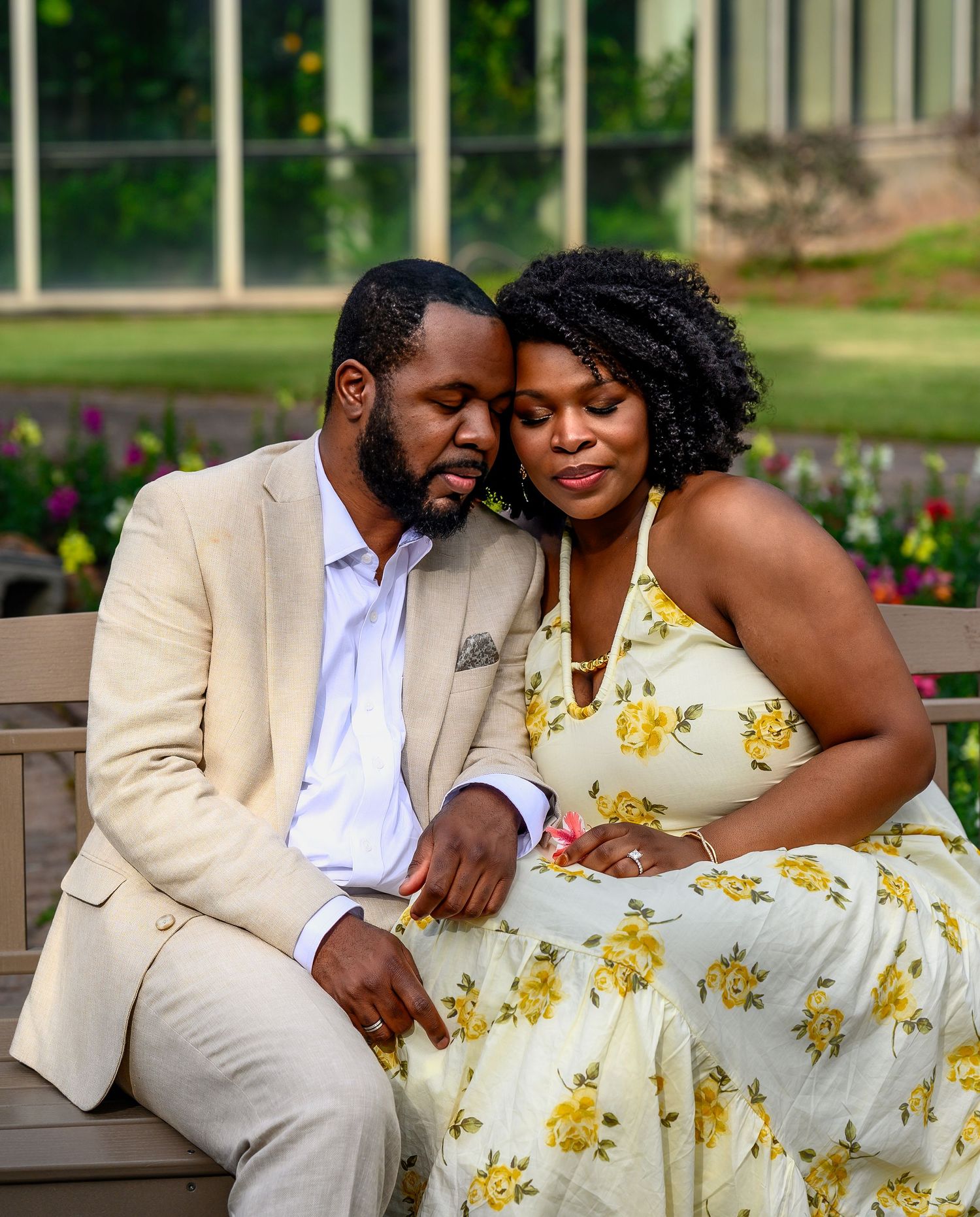 Newlywed couple sitting closely together on bench in flower garden.