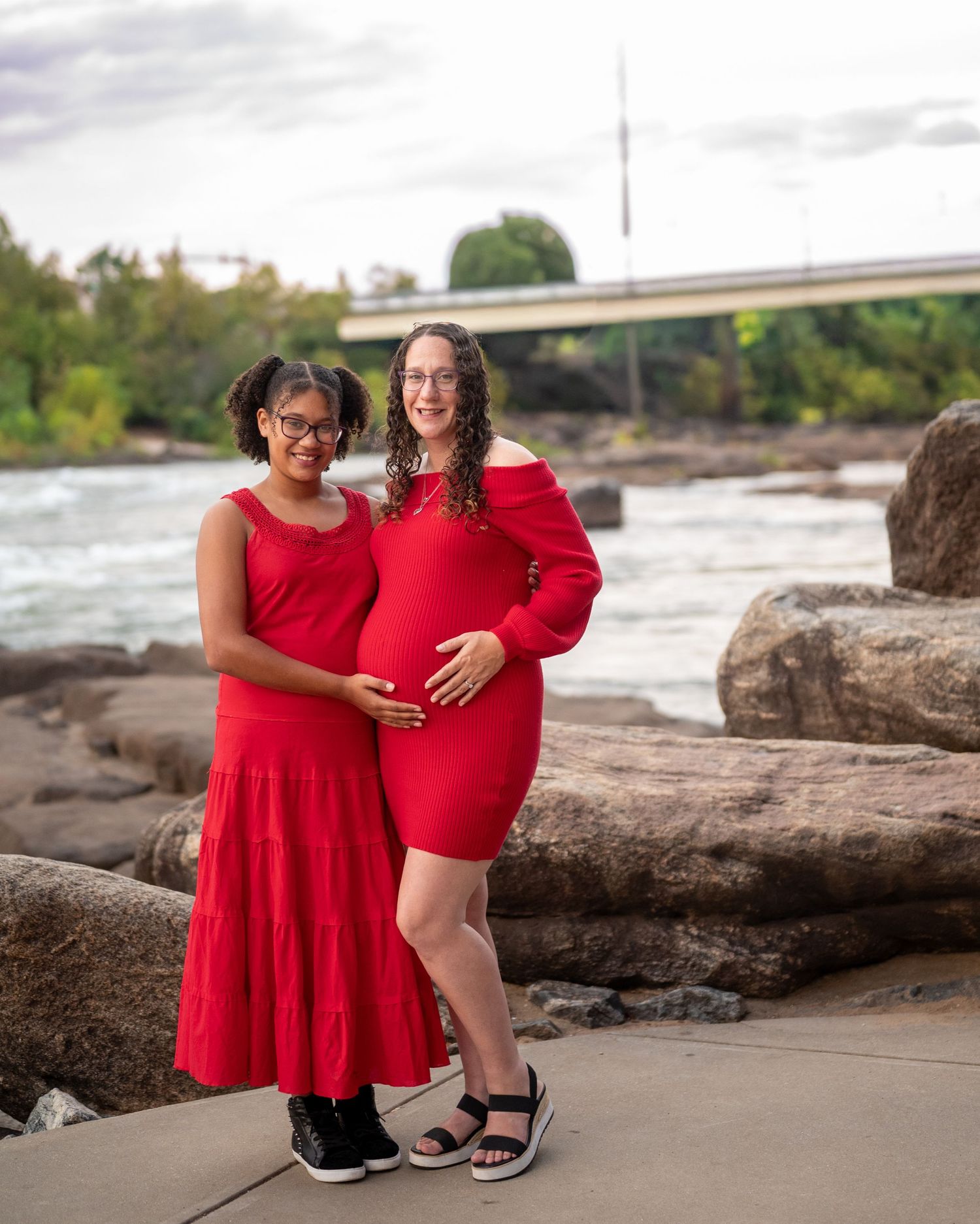Family wearing matching red outfits poses together on rocky shoreline during outdoor photoshoot.
