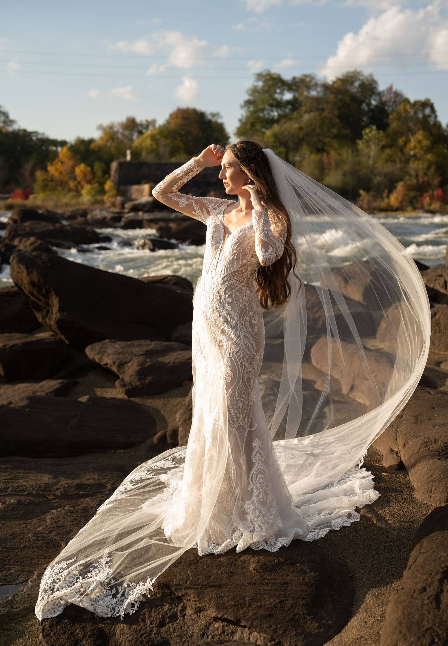Dramatic bridal pose on rocky terrain with flowing veil catching the wind at sunset.