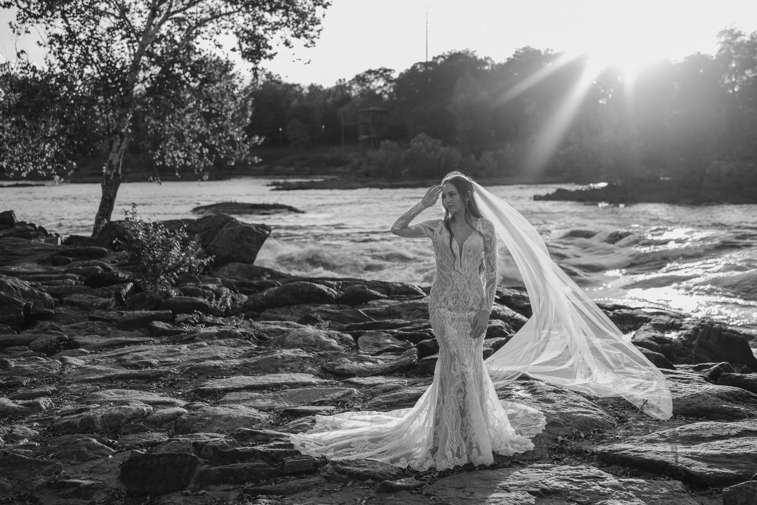 Black and white bridal photography with dramatic veil movement on rocky coastal landscape.