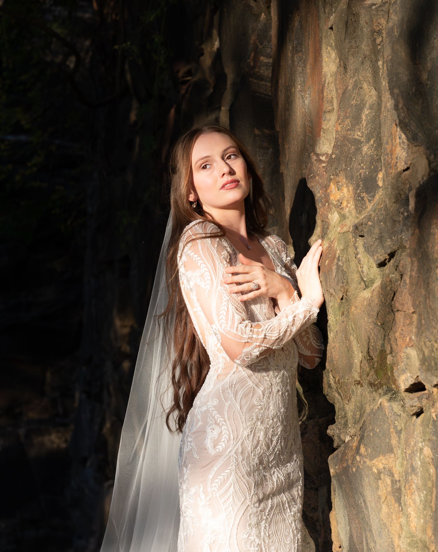 An artistic bridal portrait series with dramatic shadows and highlights against a stone wall backdrop.