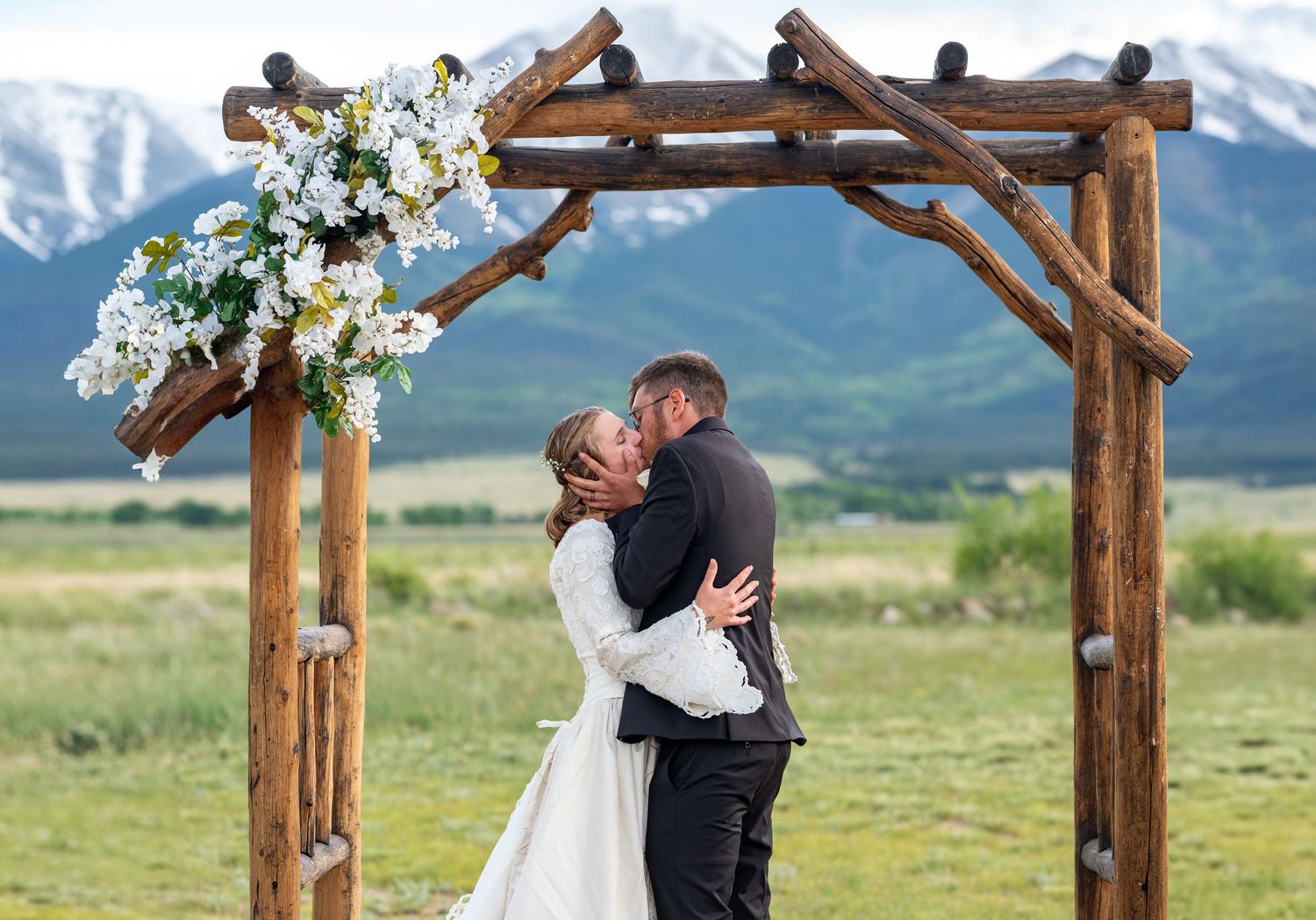 Outdoor wedding ceremony under a rustic wooden arch with mountain views in the background.