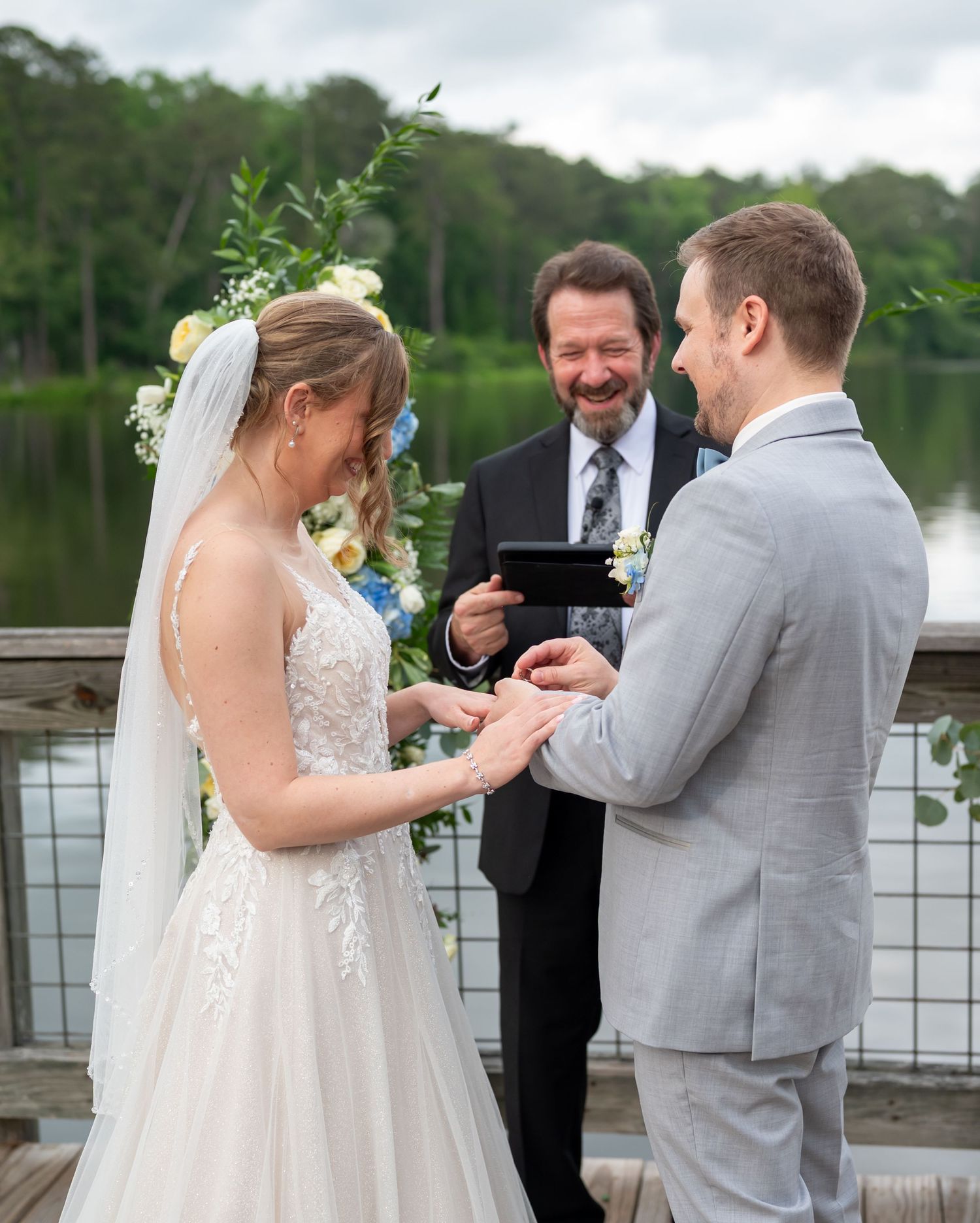 Wedding ceremony ring exchange moment captured on outdoor lakeside dock.
