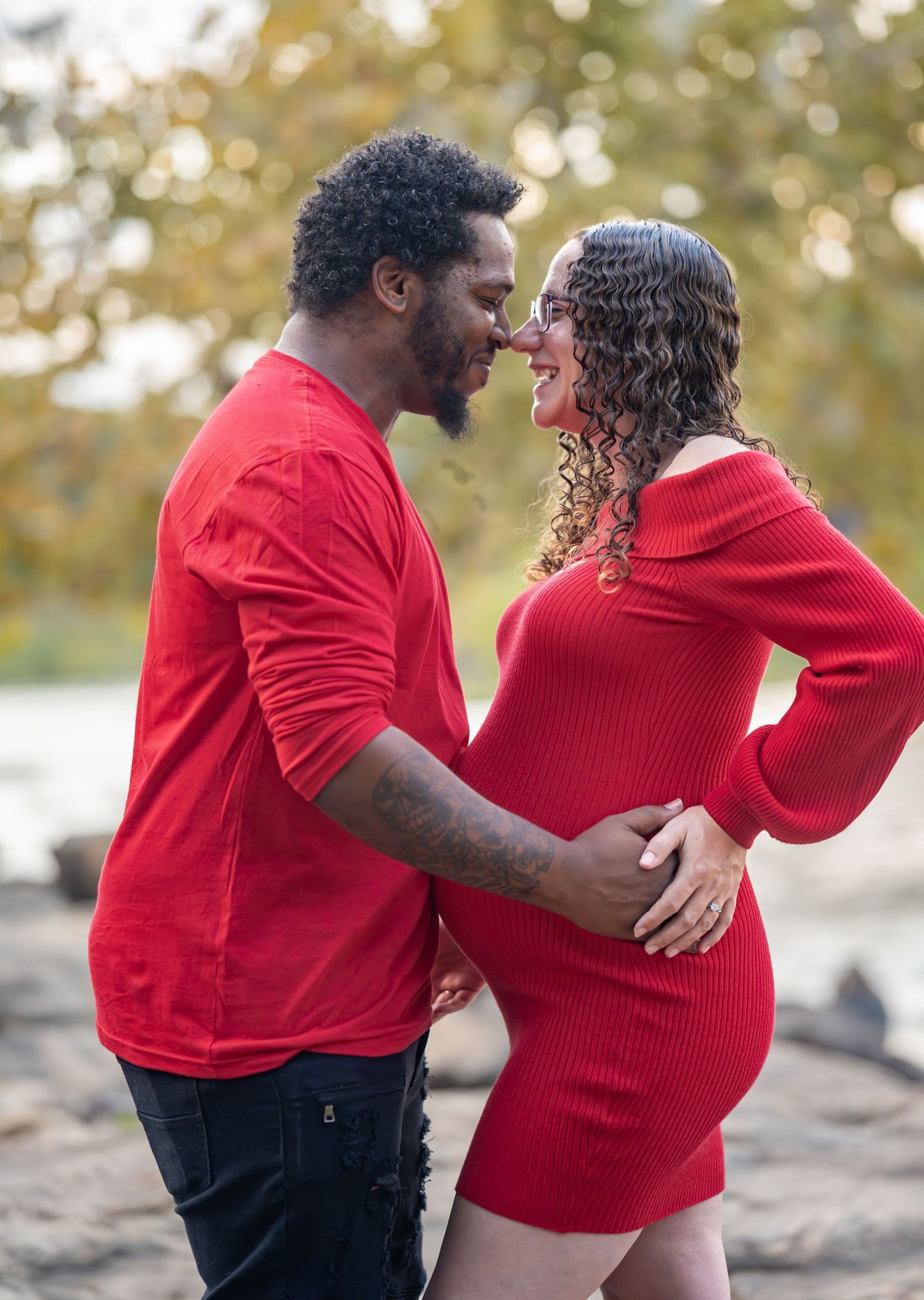 Couple in matching red outfits shares intimate moment during outdoor maternity photoshoot.
