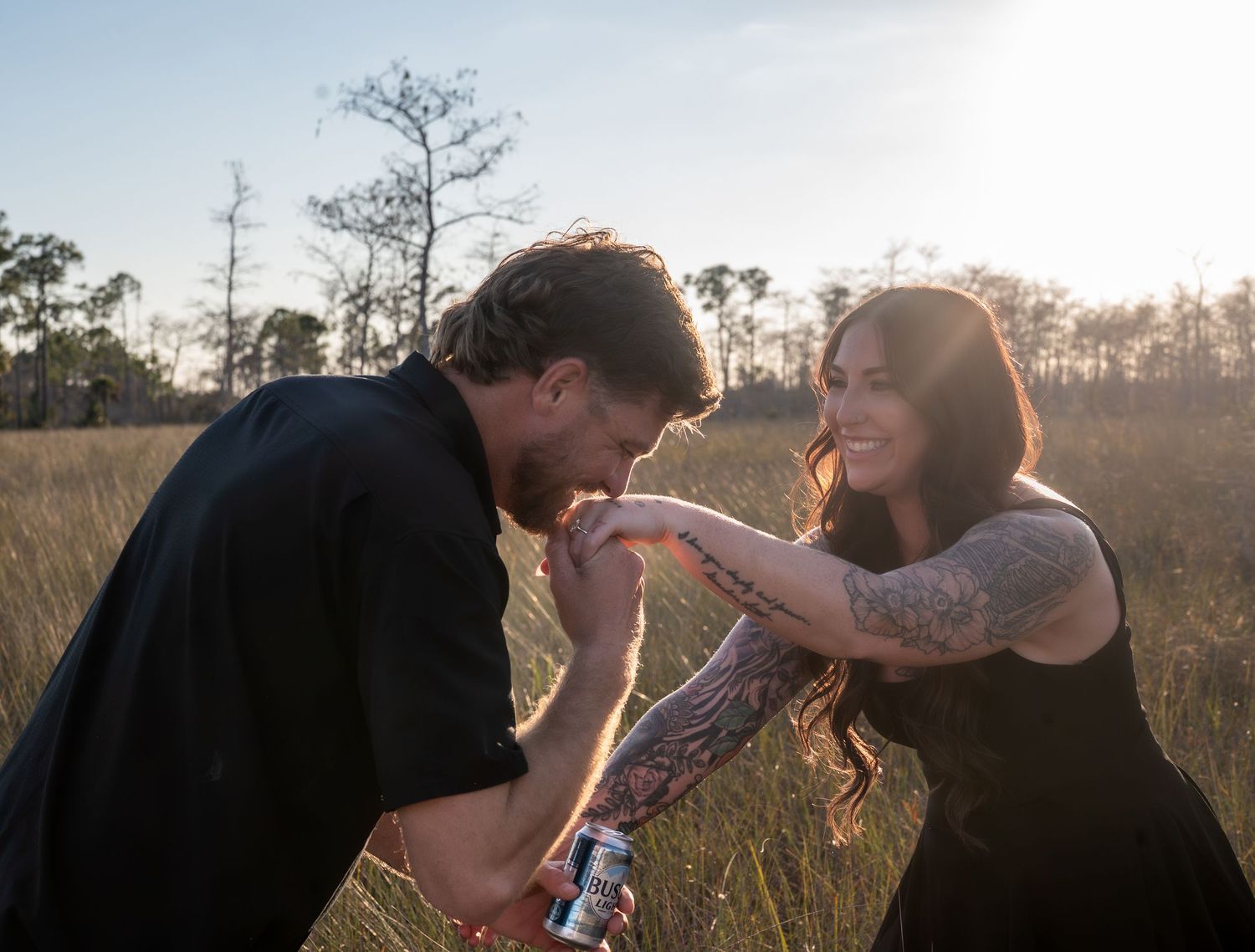 Two people share an intimate moment in a sunlit field during golden hour as the sun sets behind them.