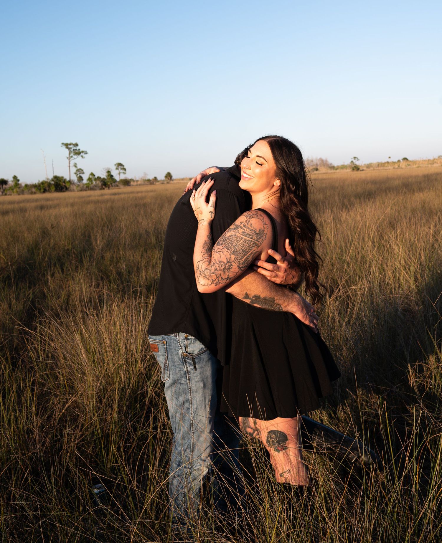 Romantic couple embracing in a field of tall grass during golden hour.