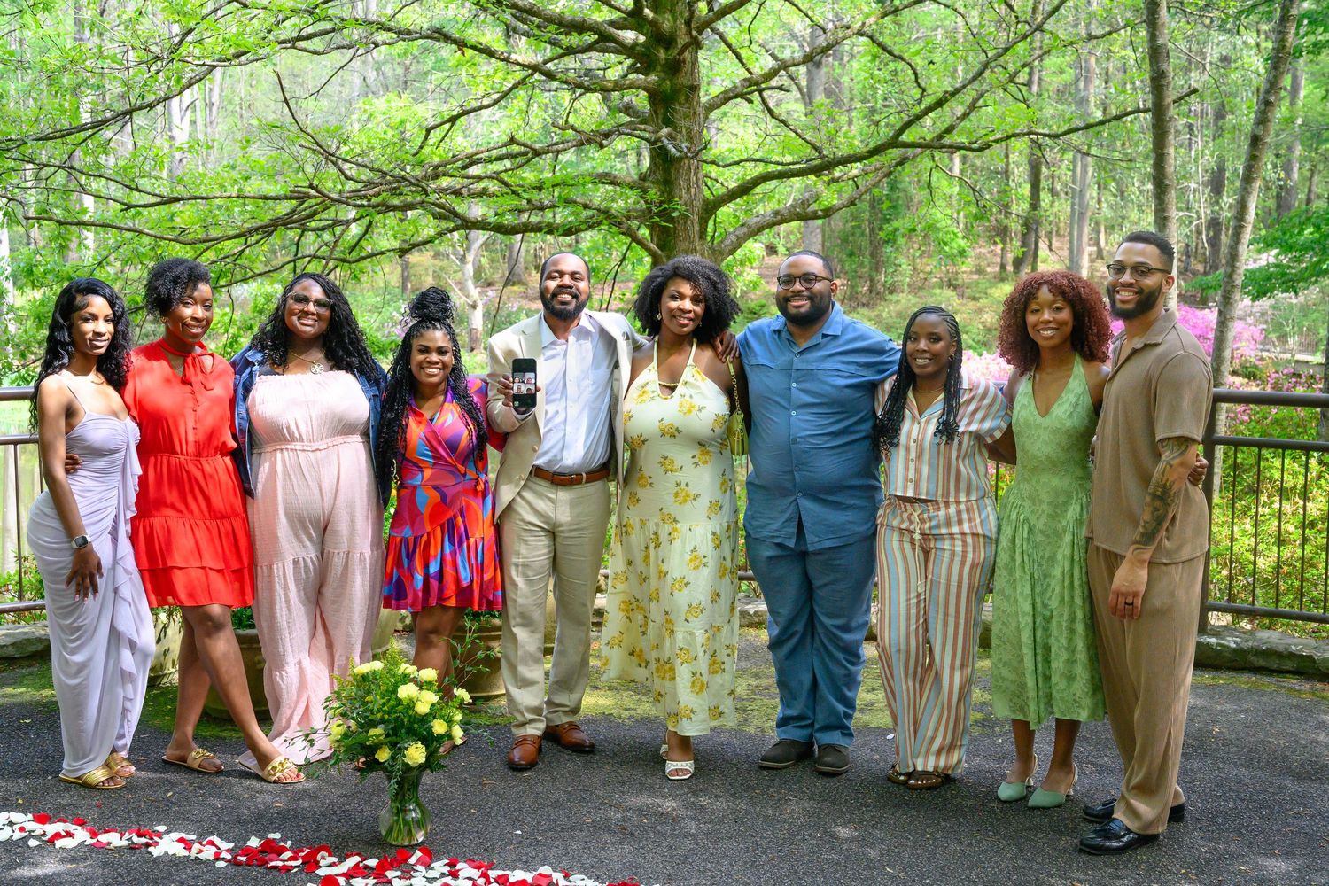 Group of ten people posing together outdoors on a garden terrace surrounded by blooming spring trees.