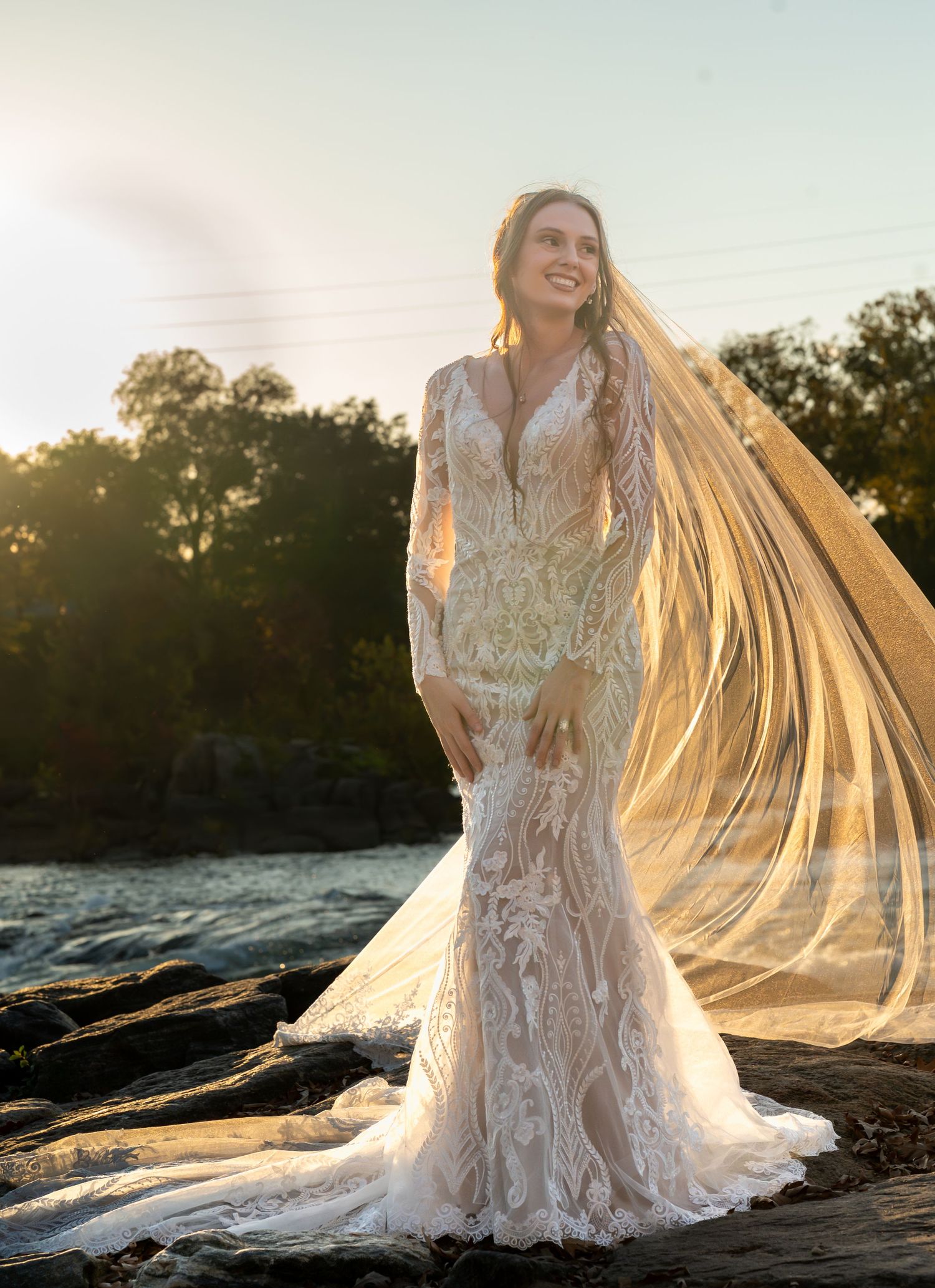 Ethereal bridal photos at sunset with a flowing cathedral veil on a rocky beach.