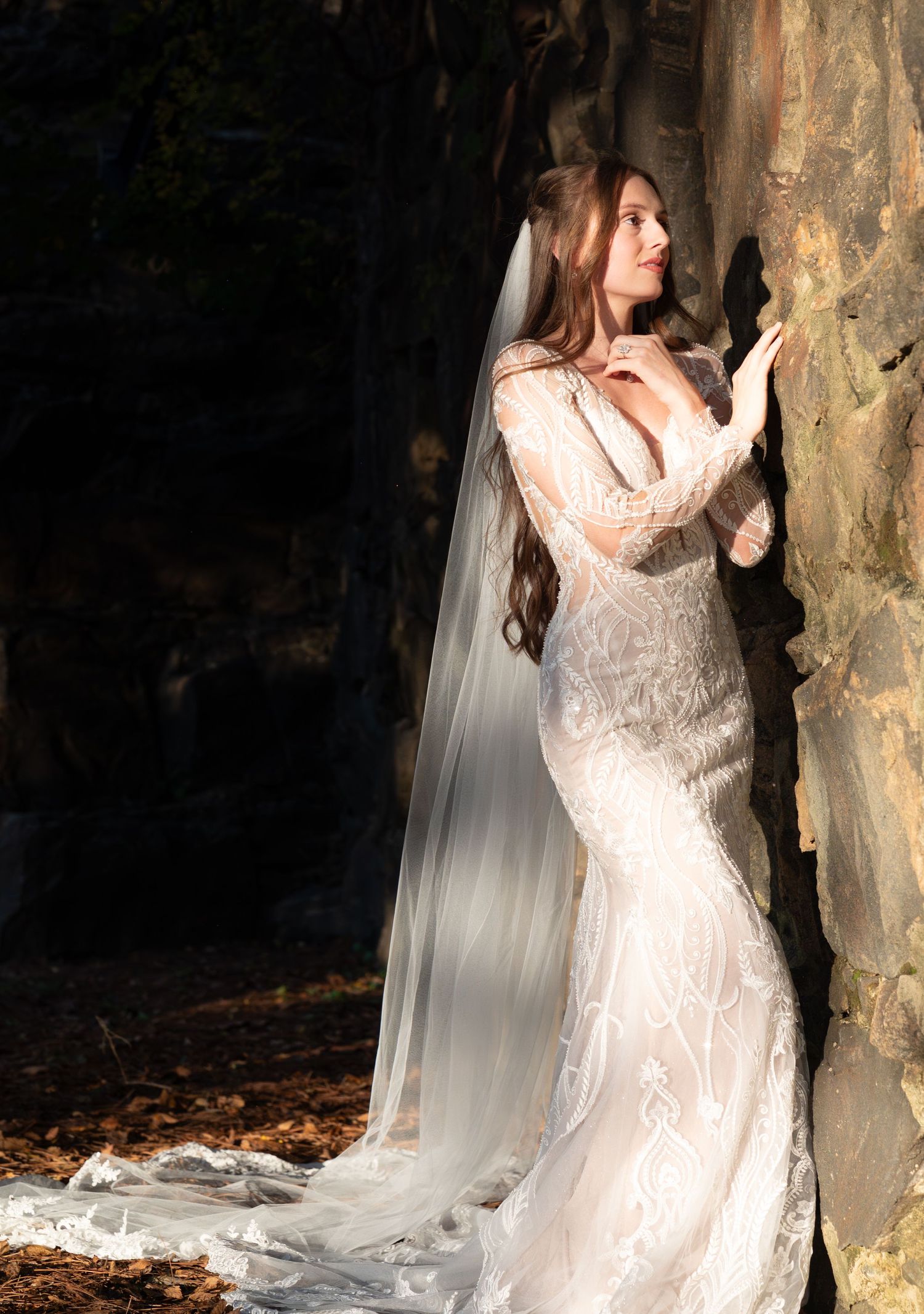 Dramatic bridal photo series showing flowing lace dress against dark stone backdrop.