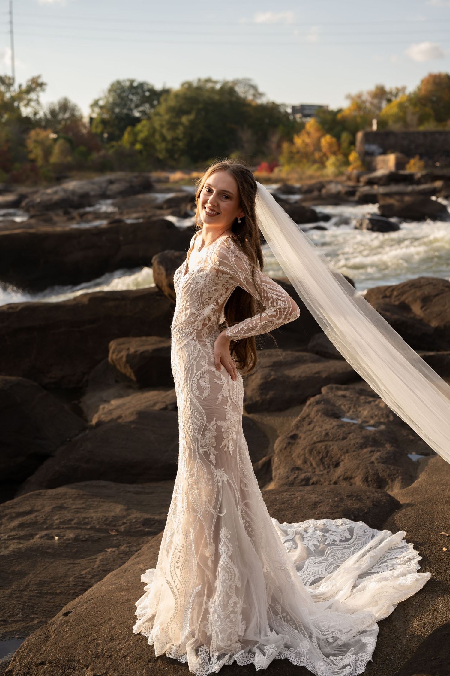 A flowing lace wedding dress with long sleeves photographed against rocky terrain at sunset.