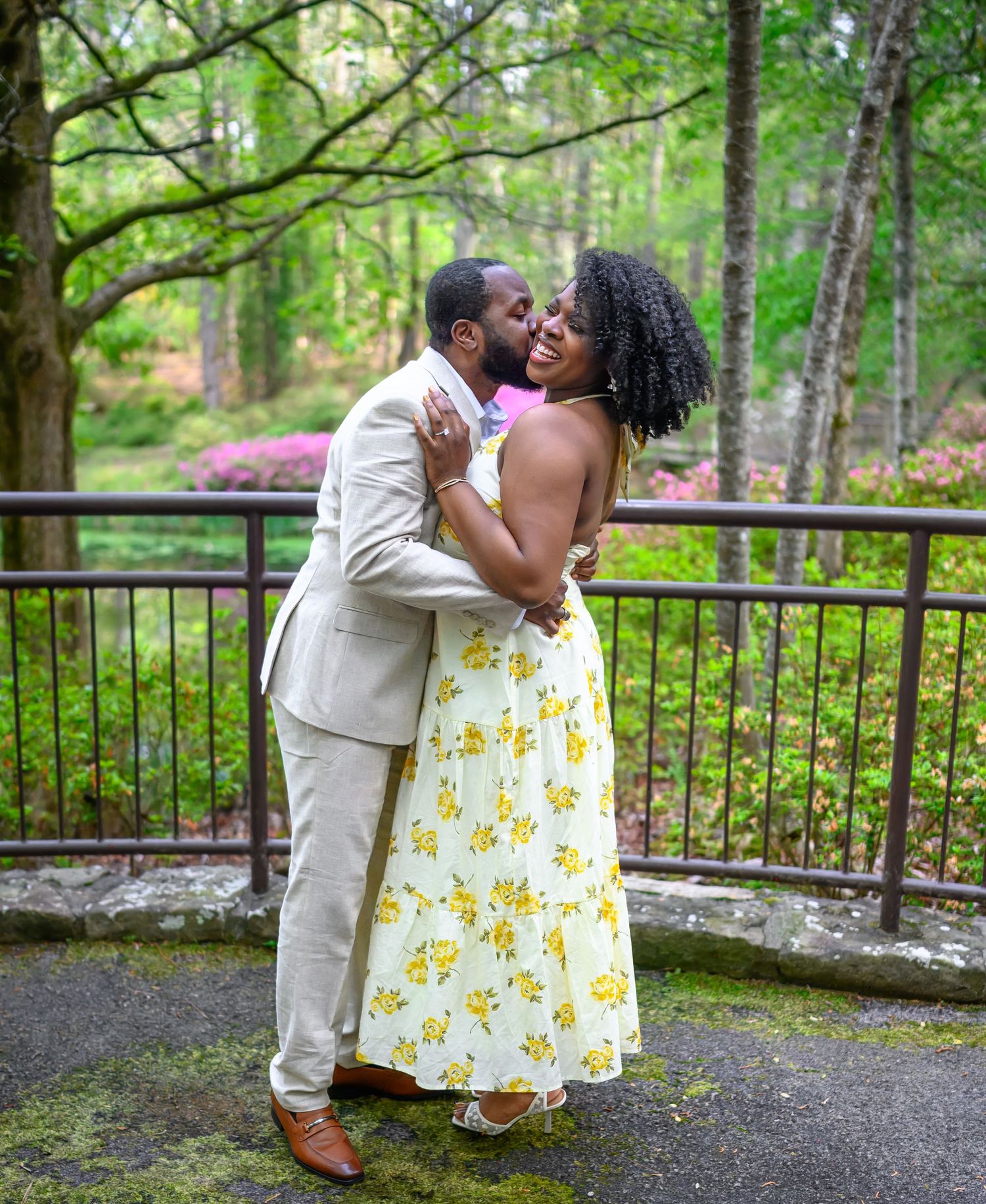 Happy couple shares a romantic kiss while embracing on a garden patio surrounded by lush green trees.