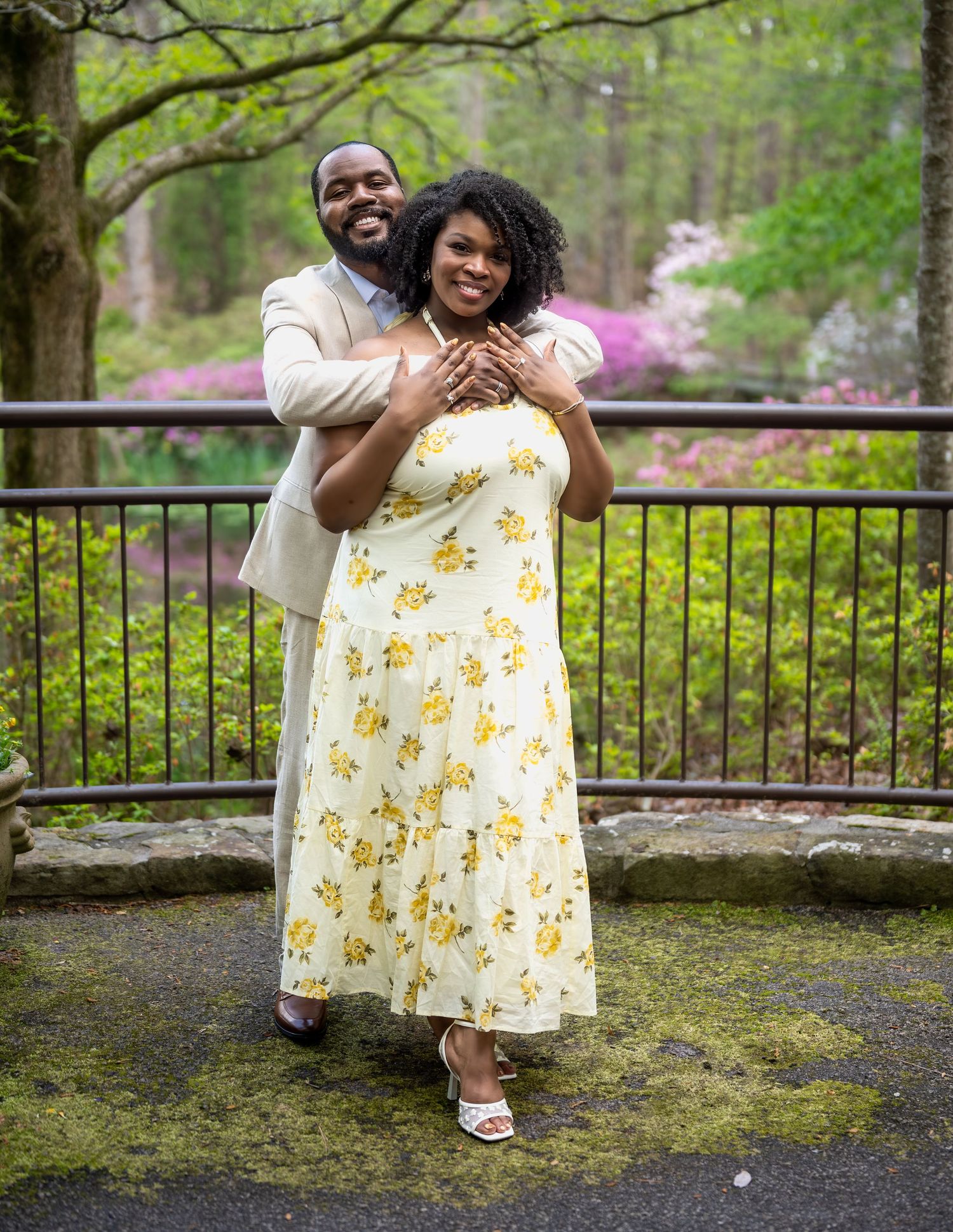 Smiling couple posing together on a mossy terrace with man hugging woman from behind.