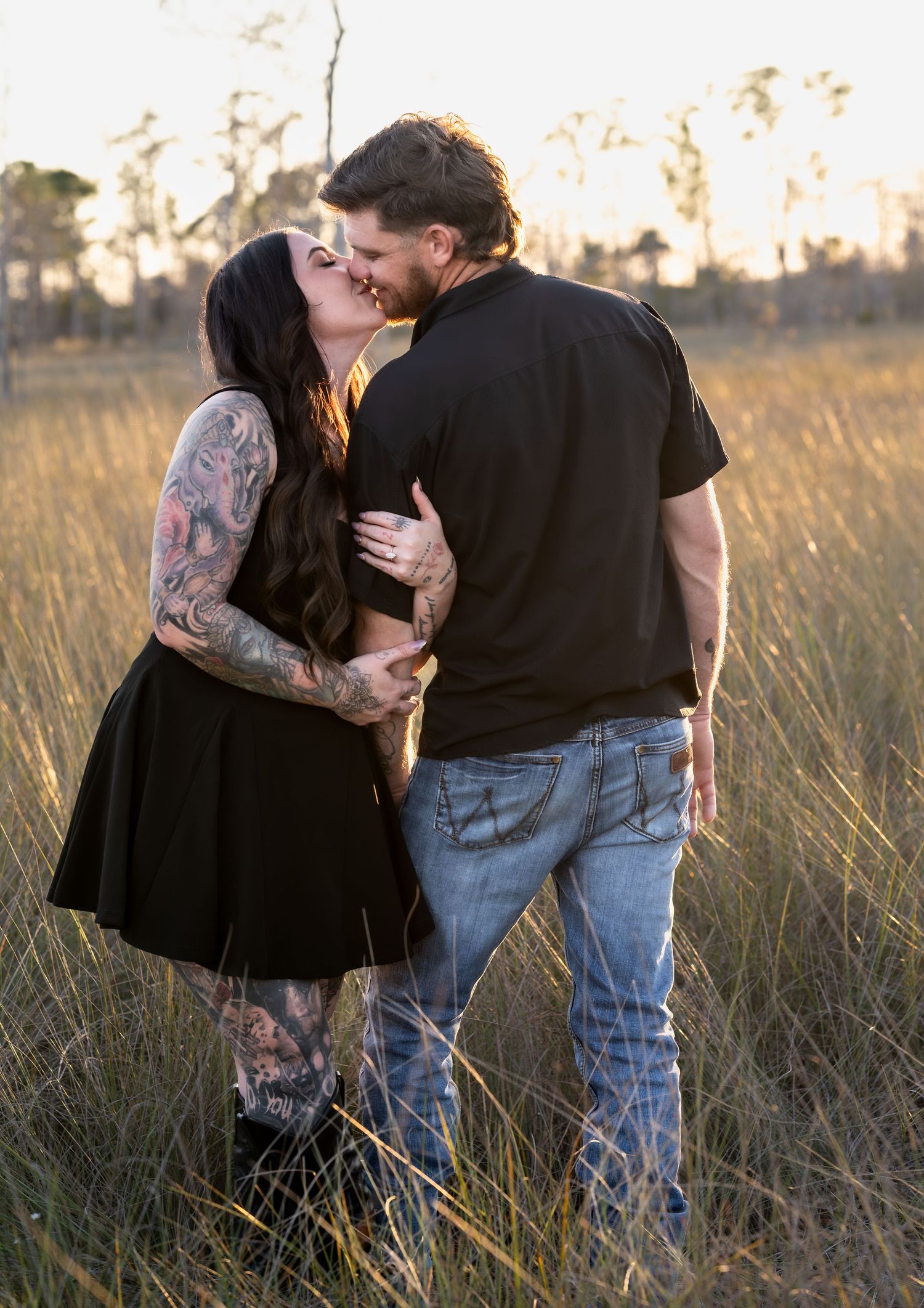 Couple shares tender moments during outdoor engagement photoshoot in grassy field.