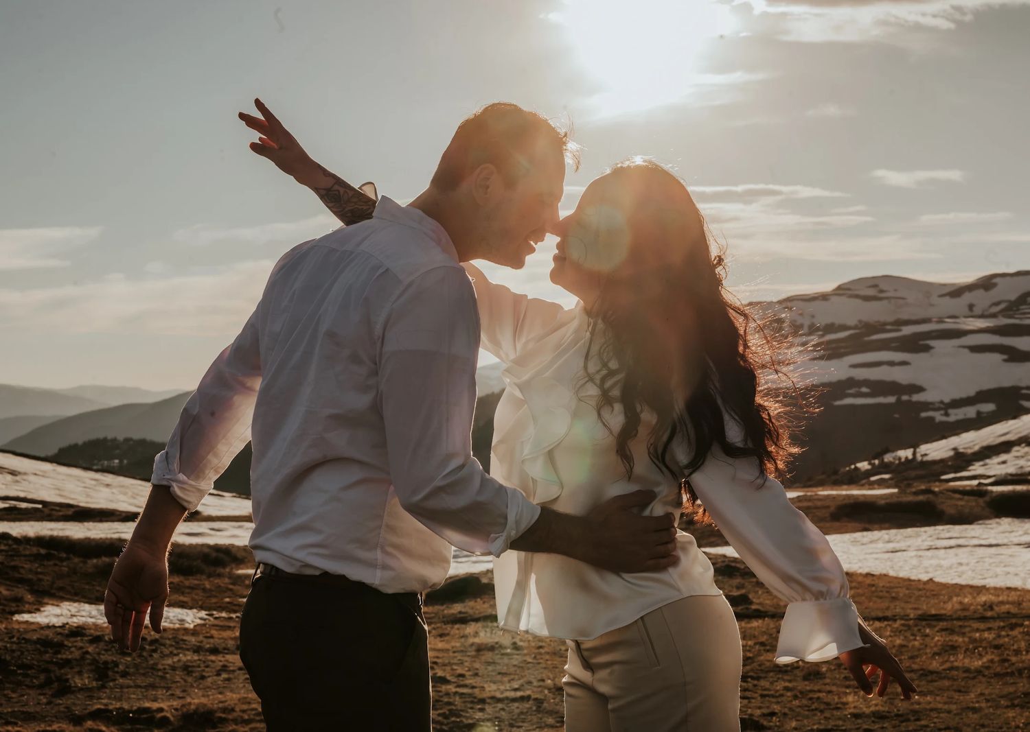 Couple dancing joyfully together against a scenic mountain landscape at sunset.