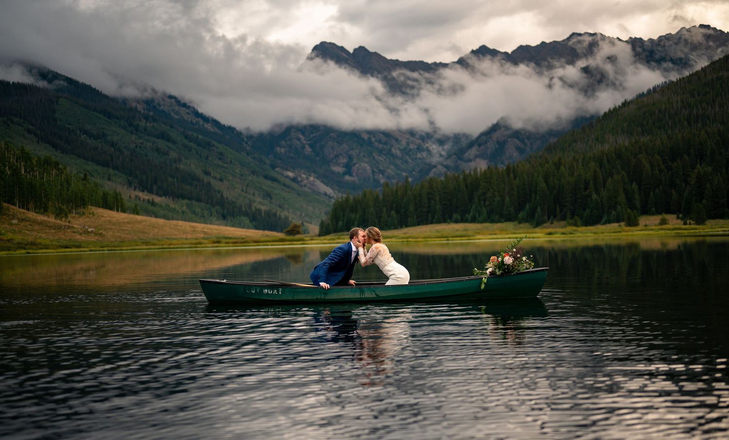 Dramatic mountain lake wedding photography with couple in canoe at sunset.
