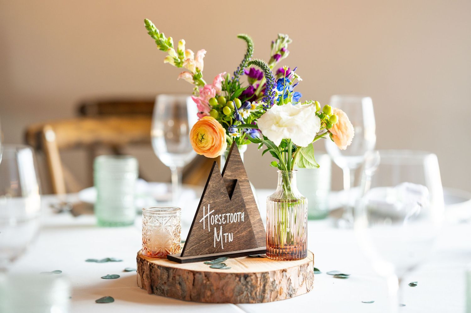 Elegant wedding table centerpiece with wood slices, flowers and glassware.