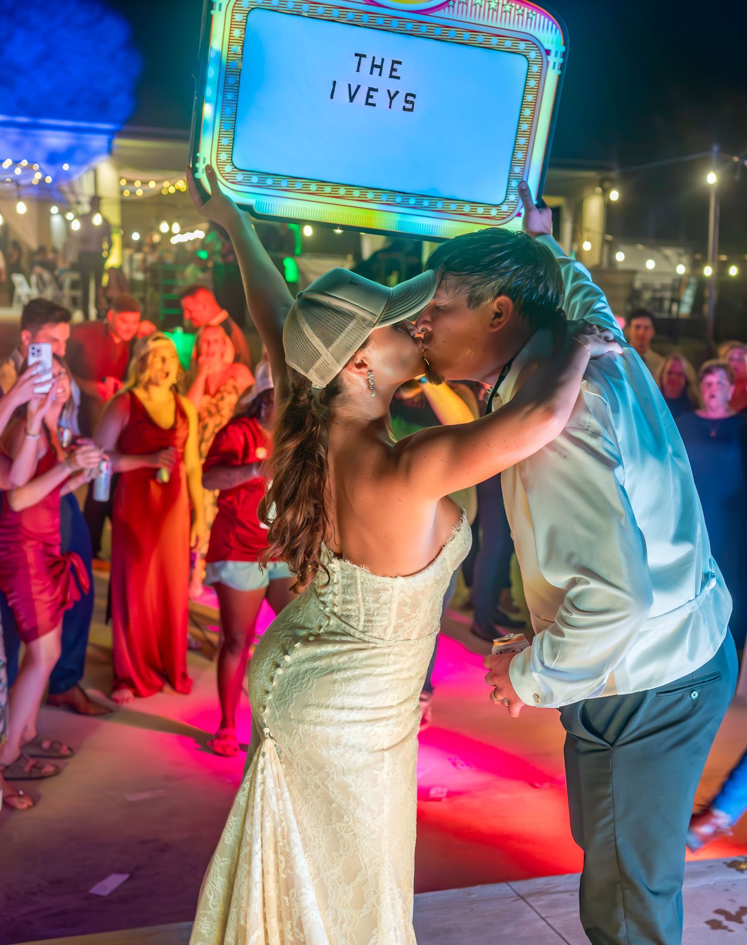 Couple shares romantic dance under neon sign at evening wedding reception.