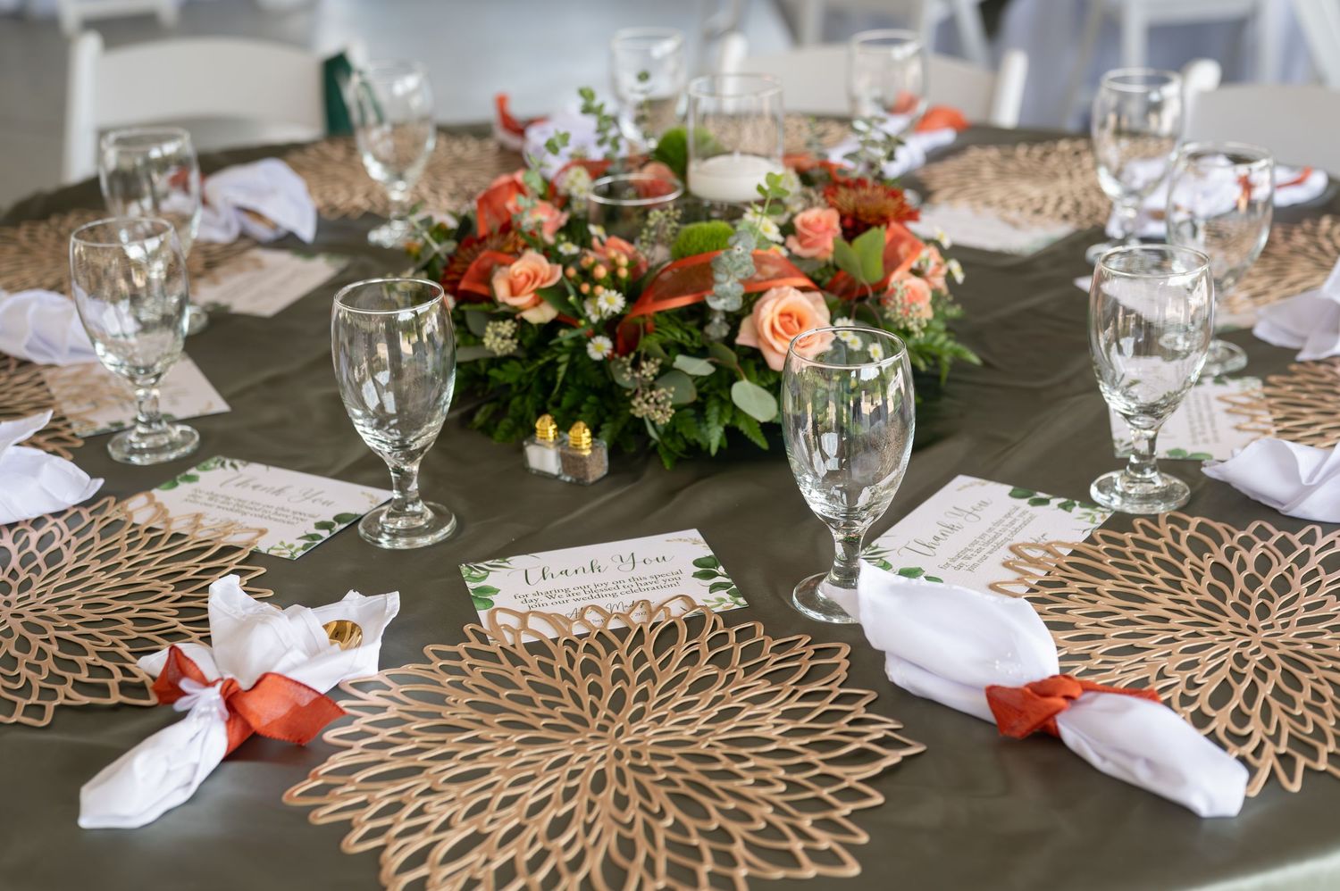 Elegant table settings with gold charger plates, wine glasses, and coral floral centerpieces at a formal dining event.