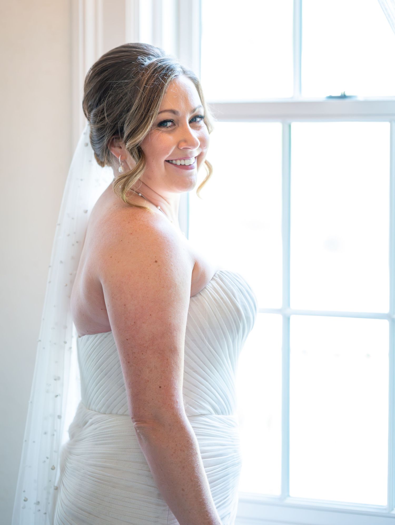 Bridal portrait sequence by bright window showing elegant white wedding dress.