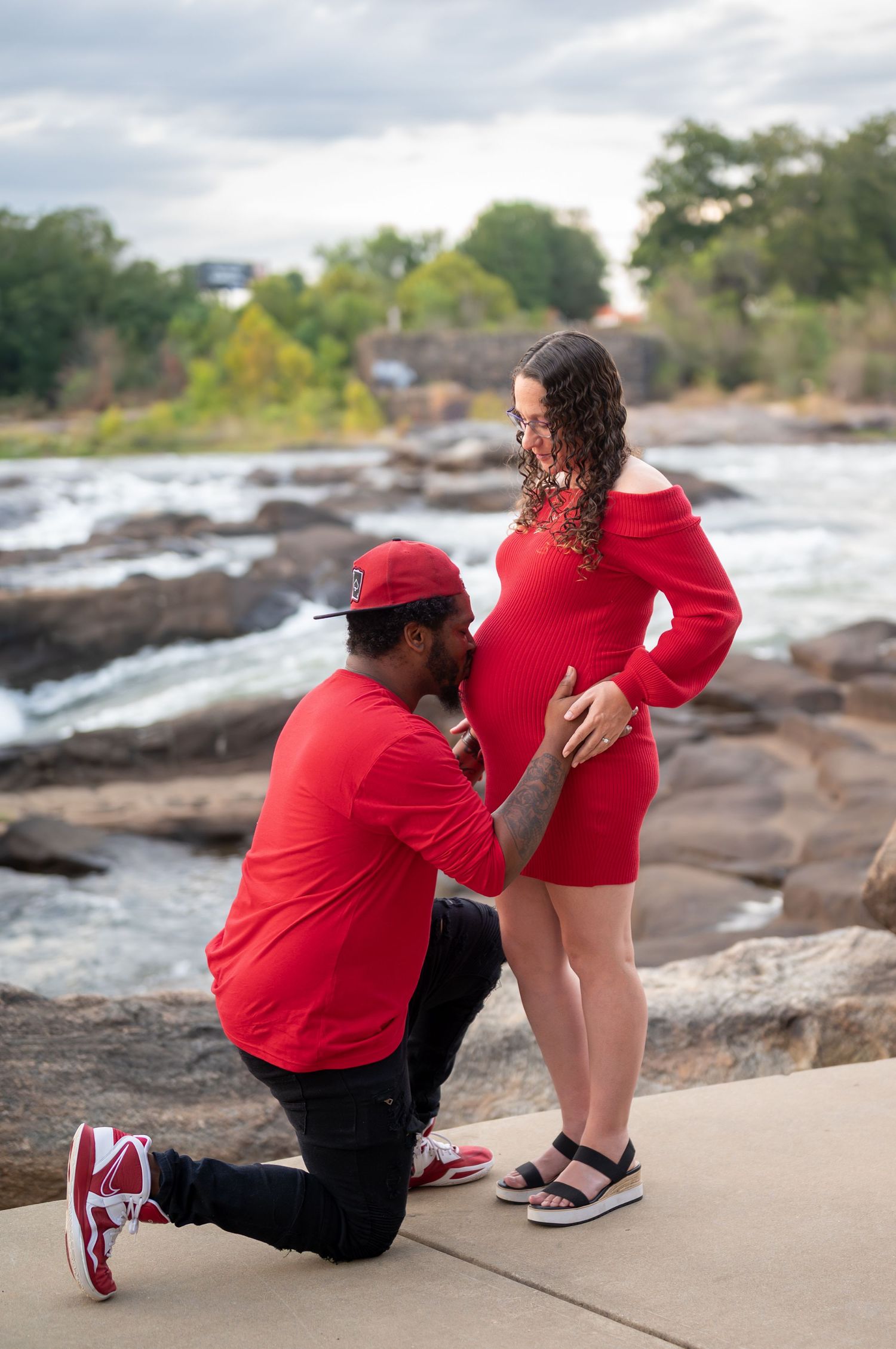 A romantic proposal scene on rocky riverbank with couple wearing matching red outfits.