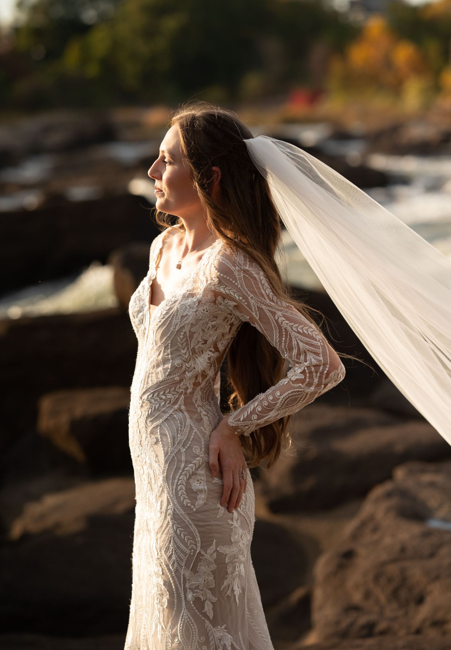 Romantic bridal photography featuring intricate lace details and flowing veil by the water.