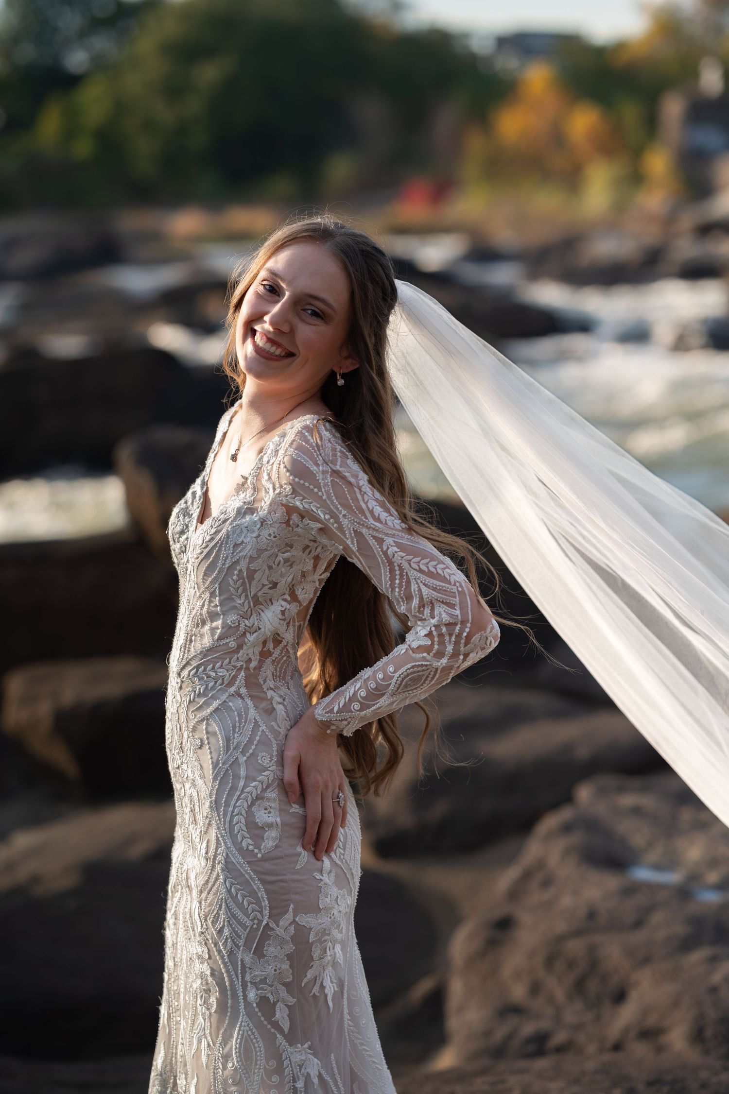 A wedding dress photoshoot on rocky terrain with flowing veil and lace details at sunset.