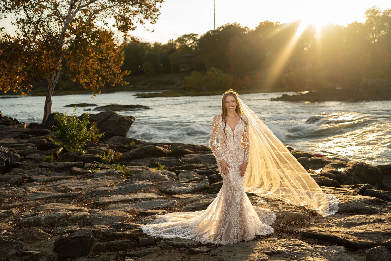 A sunset bridal photo shoot on rocky terrain near water with a dramatic cathedral-length veil.