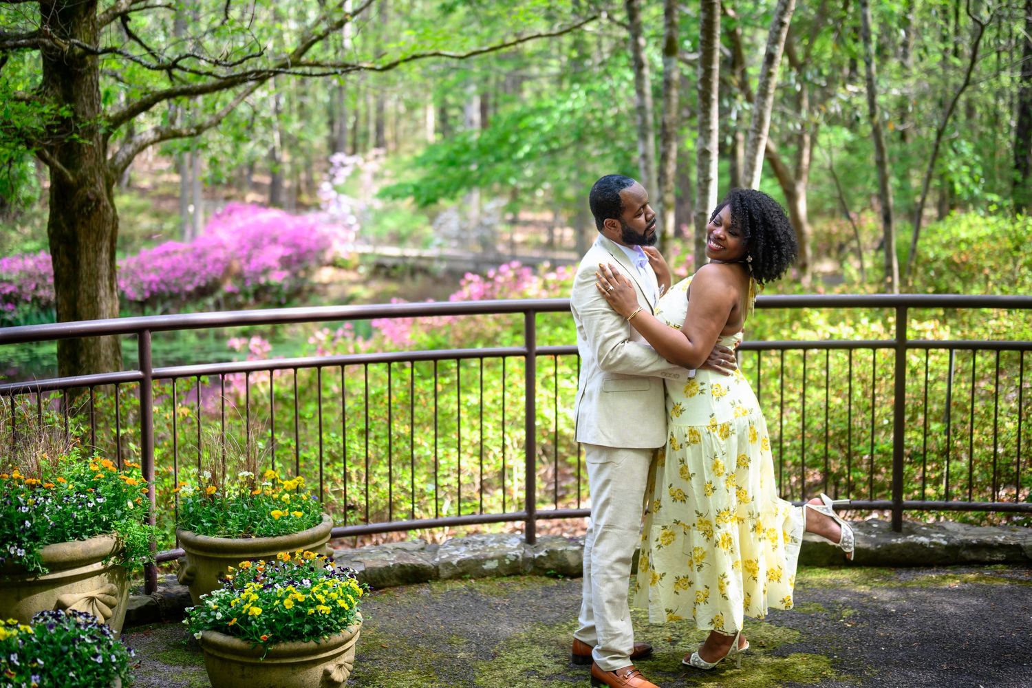 Couple embracing on a garden terrace surrounded by blooming azaleas and lush greenery.
