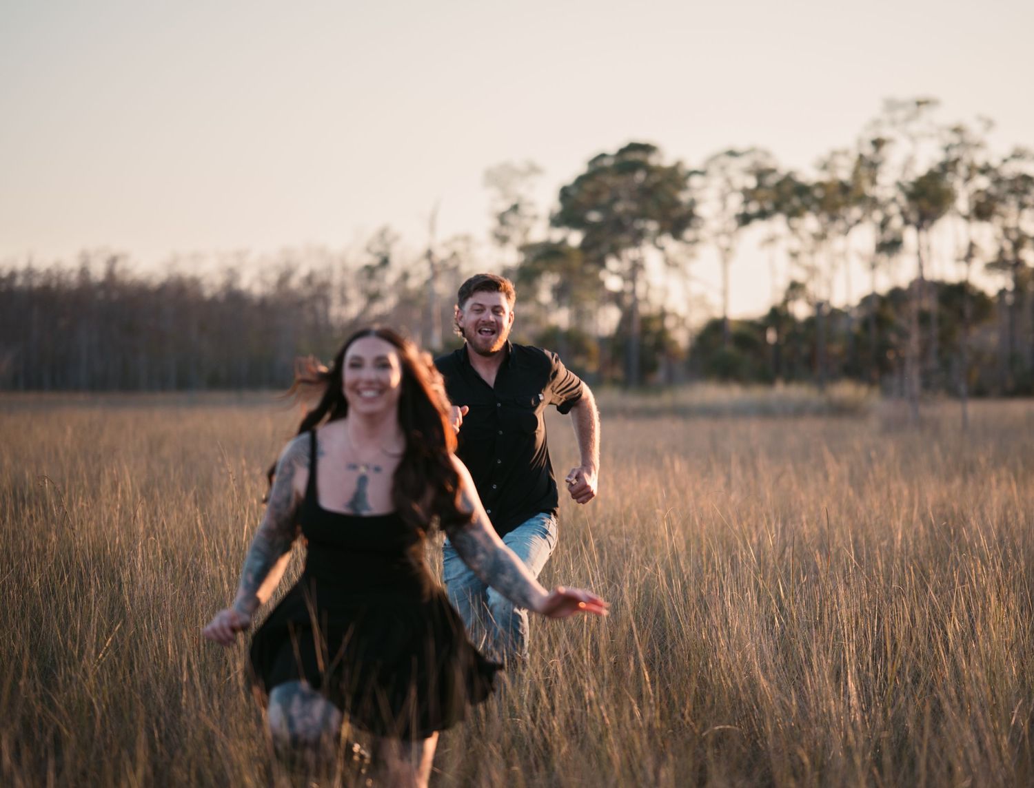 Two people running joyfully through a golden field at sunset with tall grass surrounding them.