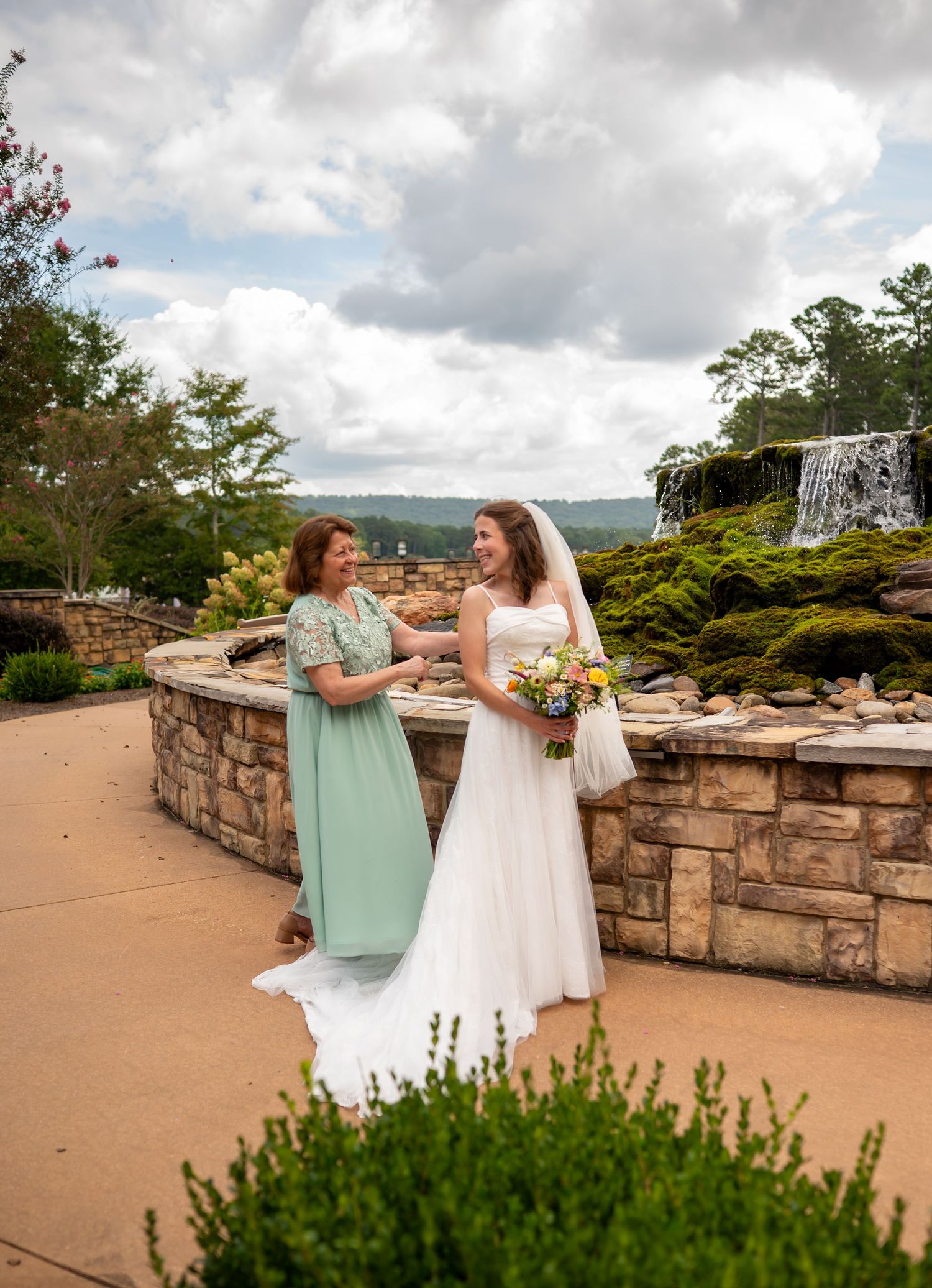 Two people share a joyful moment together on a scenic overlook with stone walls and cloudy skies in the background.