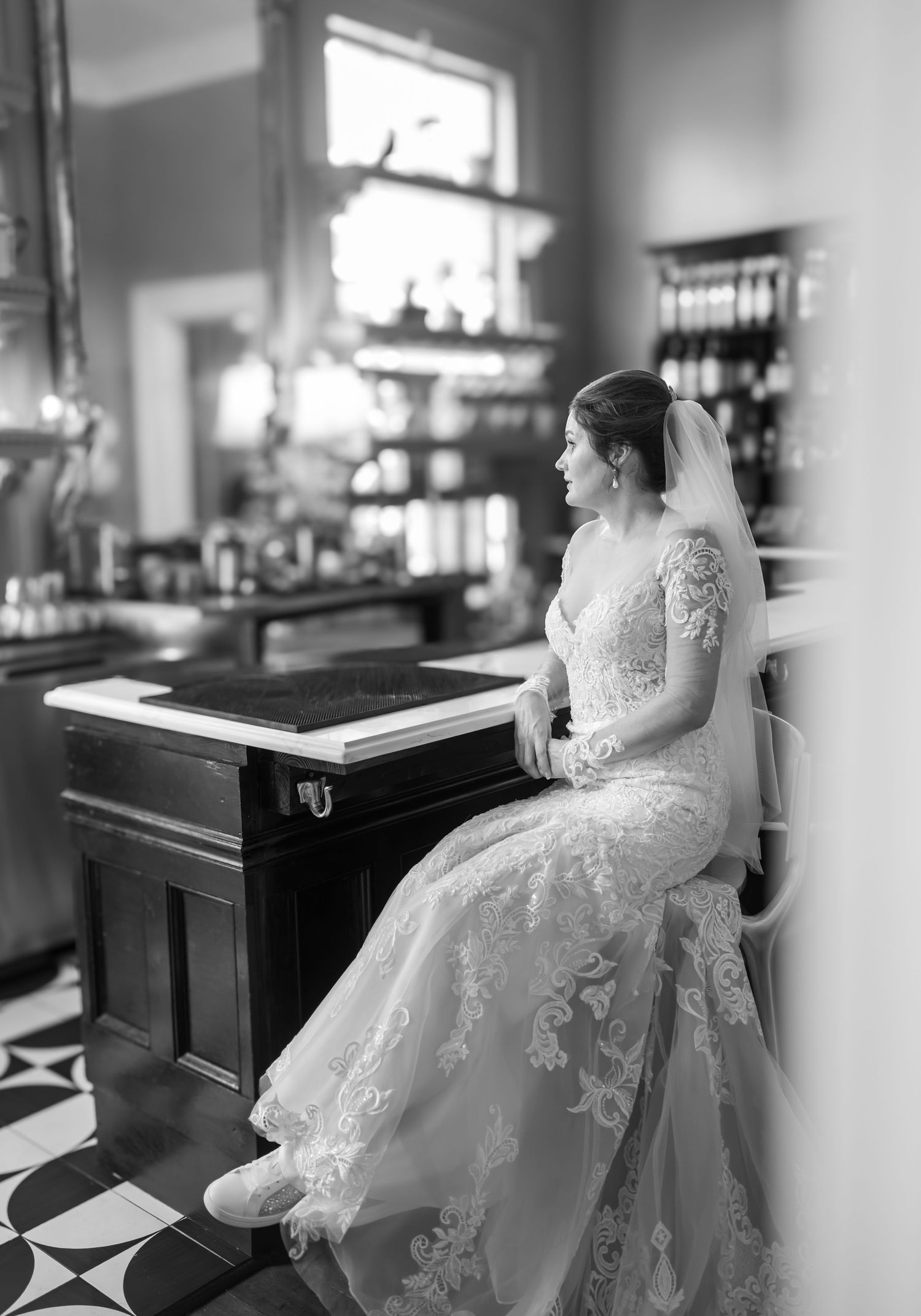 A black and white series of elegant bridal portraits showing someone in a lace wedding gown sitting at a vintage bar.