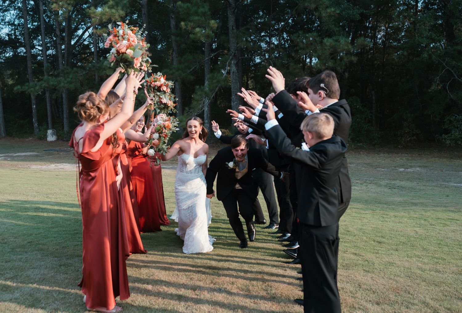 Wedding party celebrating outdoors with bridal party in rust dresses and groomsmen in black suits.