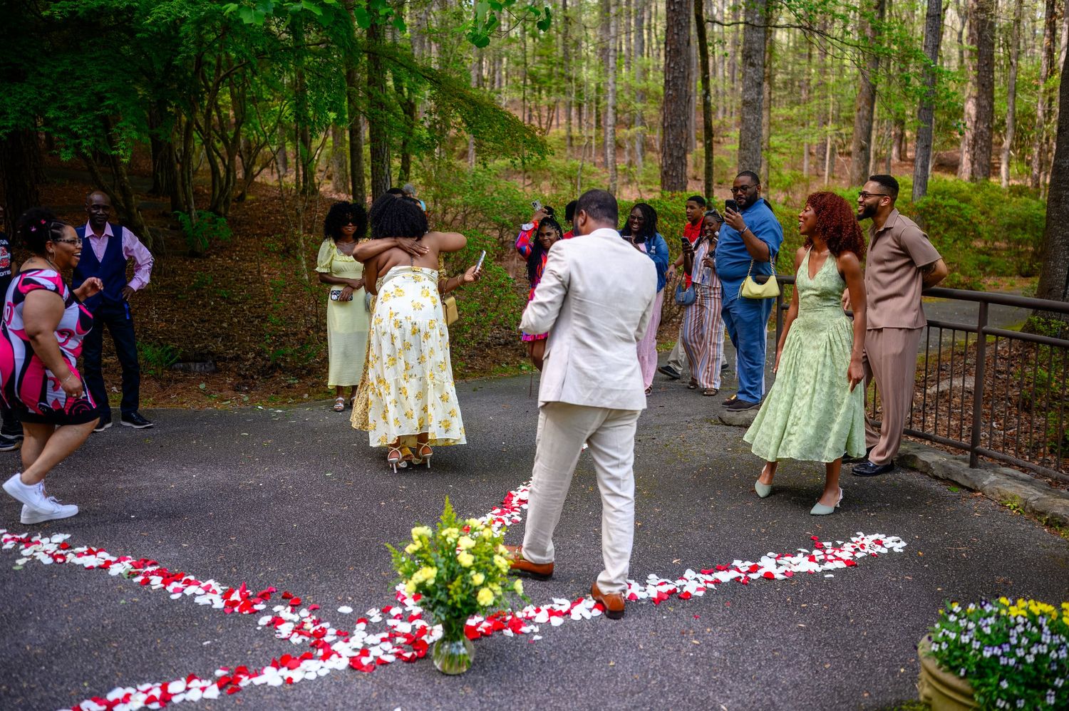Wedding guests gathering around rose petal aisle in wooded outdoor venue.