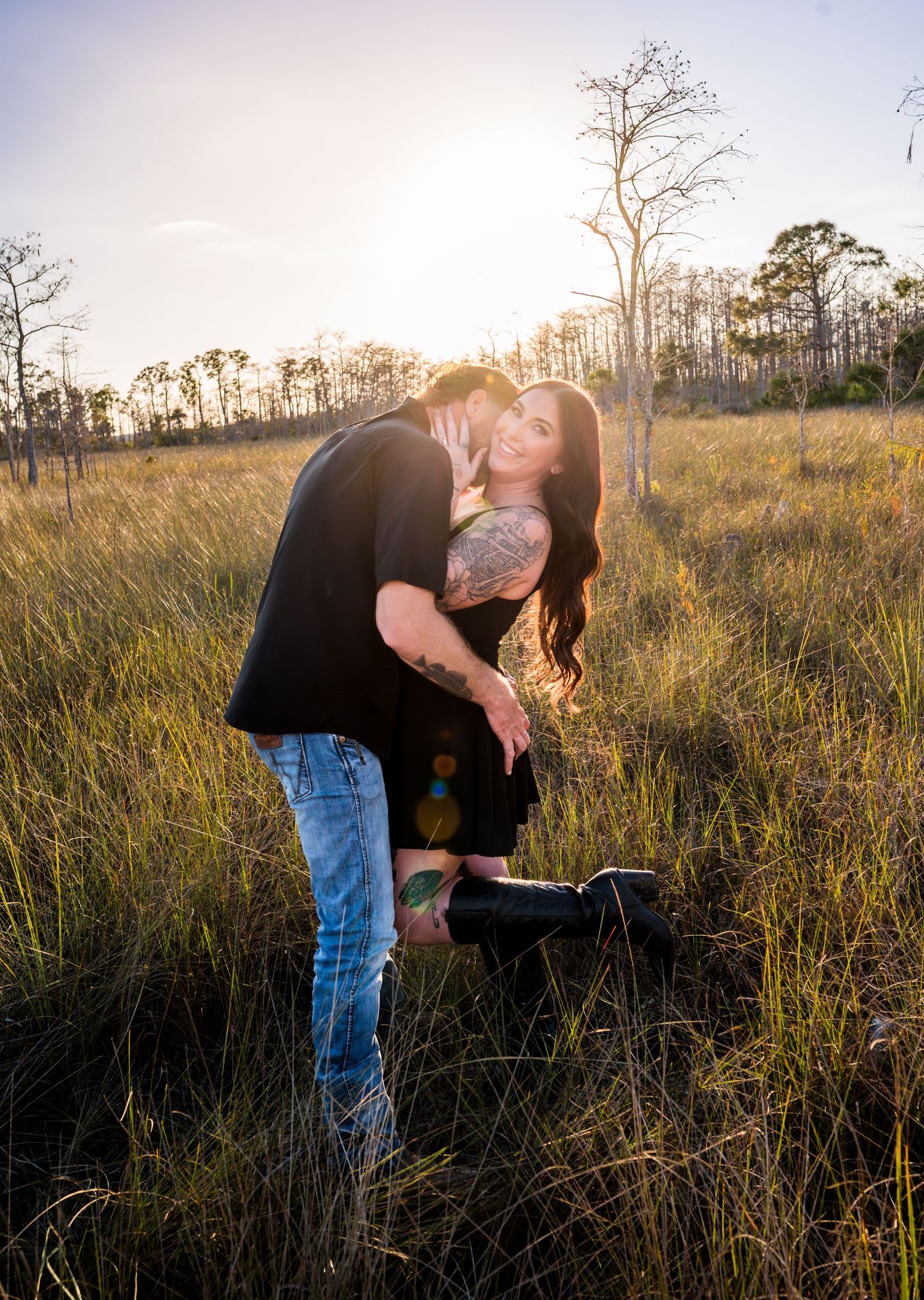 Couple shares romantic moments in a wild grass field during sunset.