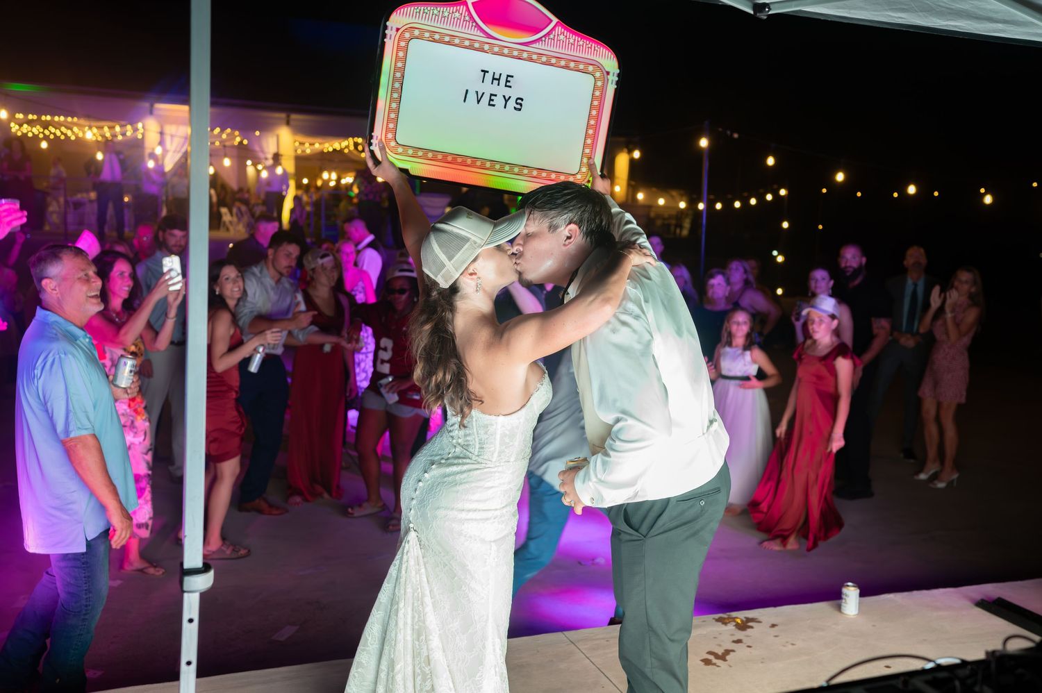A couple shares a romantic dance moment under string lights at an outdoor evening wedding reception.