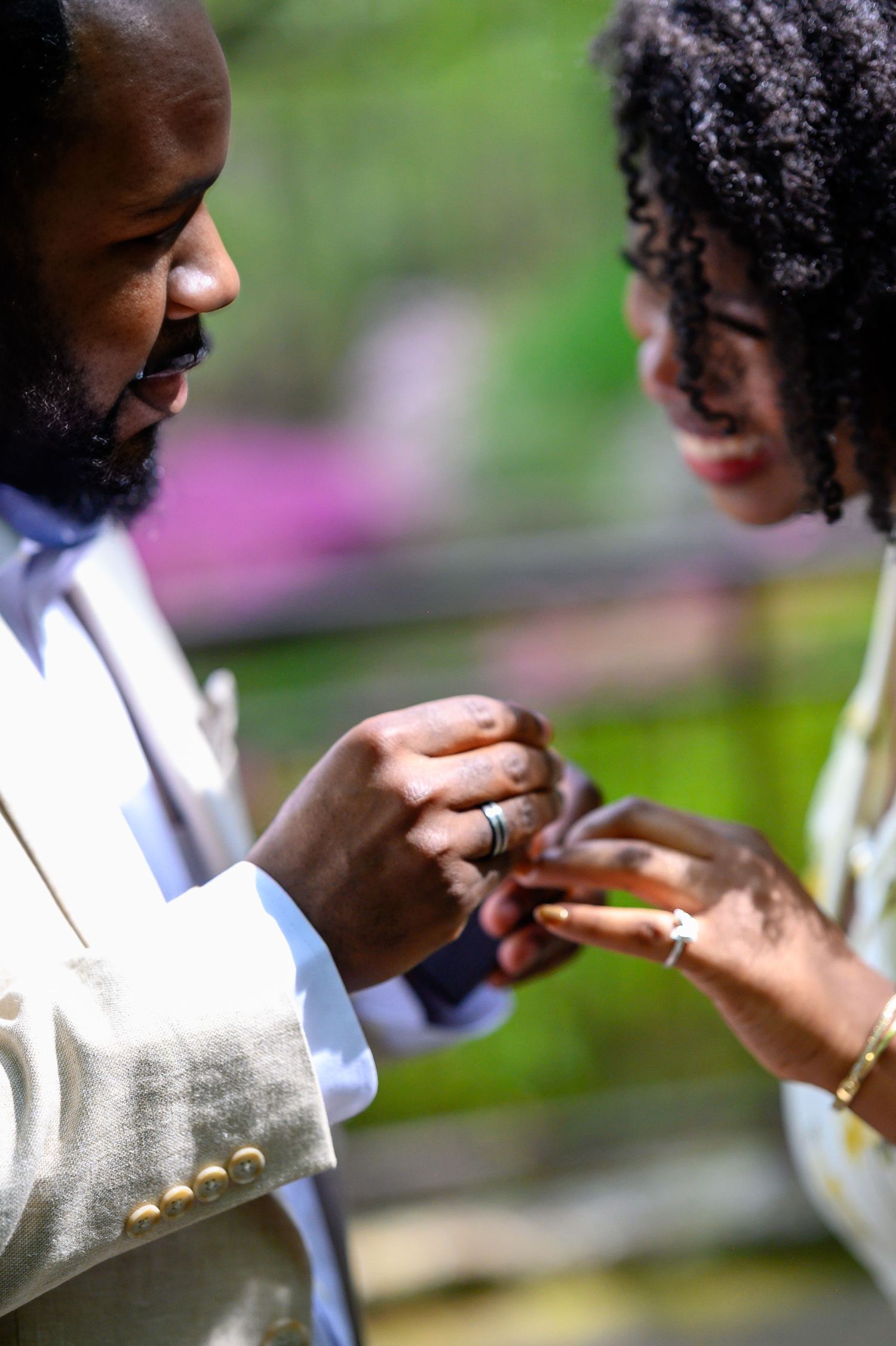 A man places an engagement ring on a woman's finger during an outdoor marriage proposal in a garden setting.