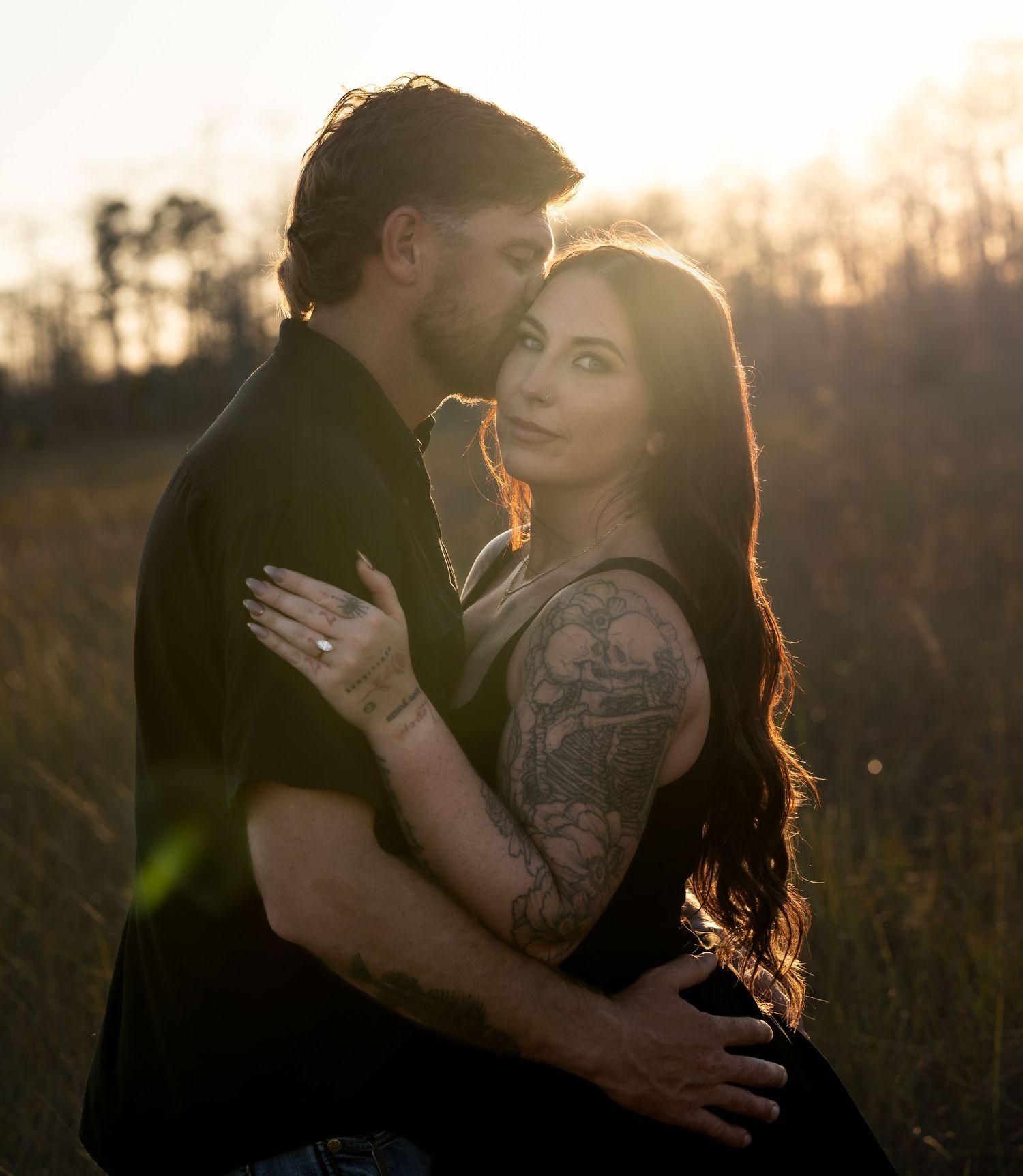 A couple embraces in a sunlit field during golden hour creating a romantic silhouette against the warm sky.