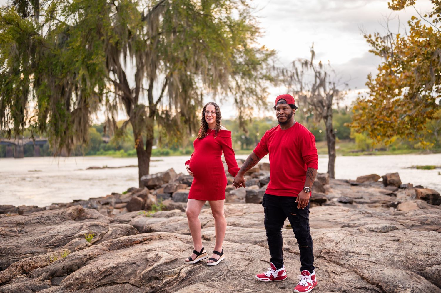 Family members walking along rocky riverbank during outdoor maternity photoshoot.
